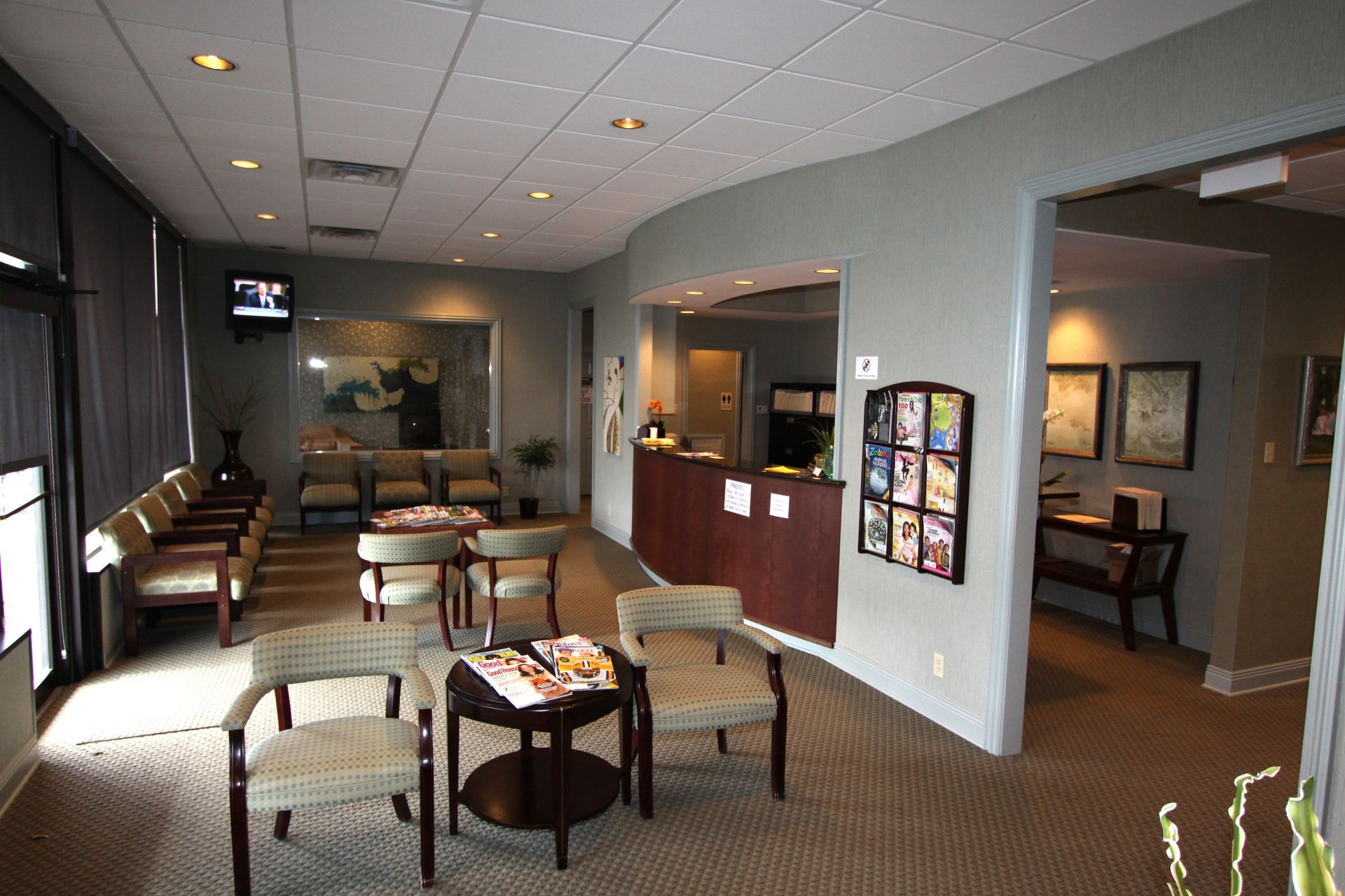 Quiet waiting room with chairs, small tables, red accent wall, and artwork under recessed lighting