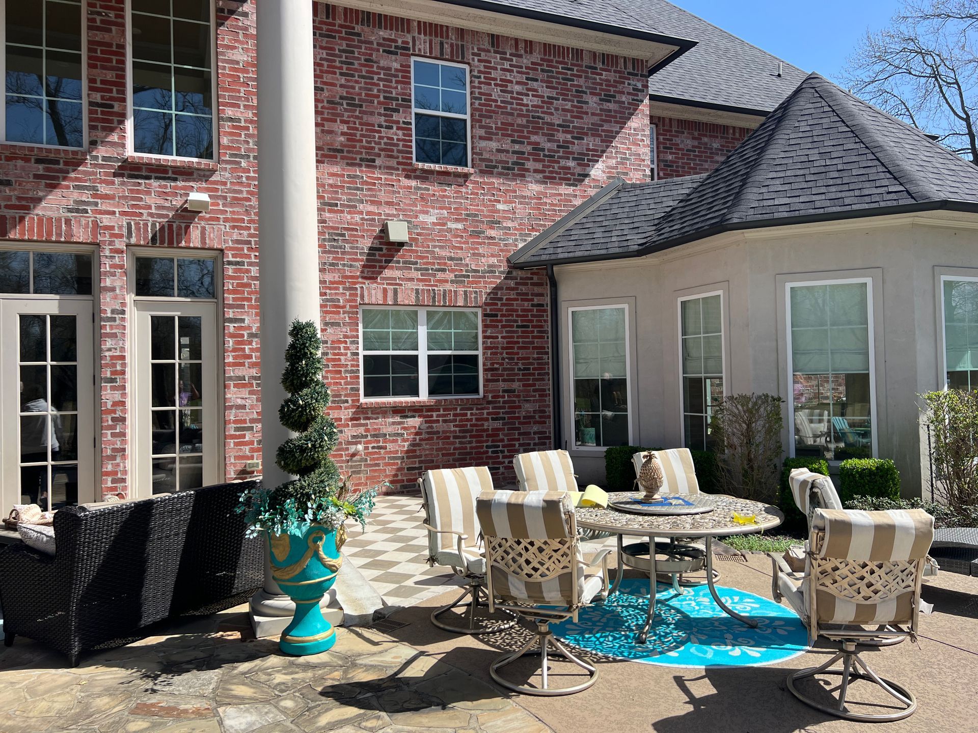 Patio with outdoor dining table, chairs, potted plants, and brick house exterior in sunlight