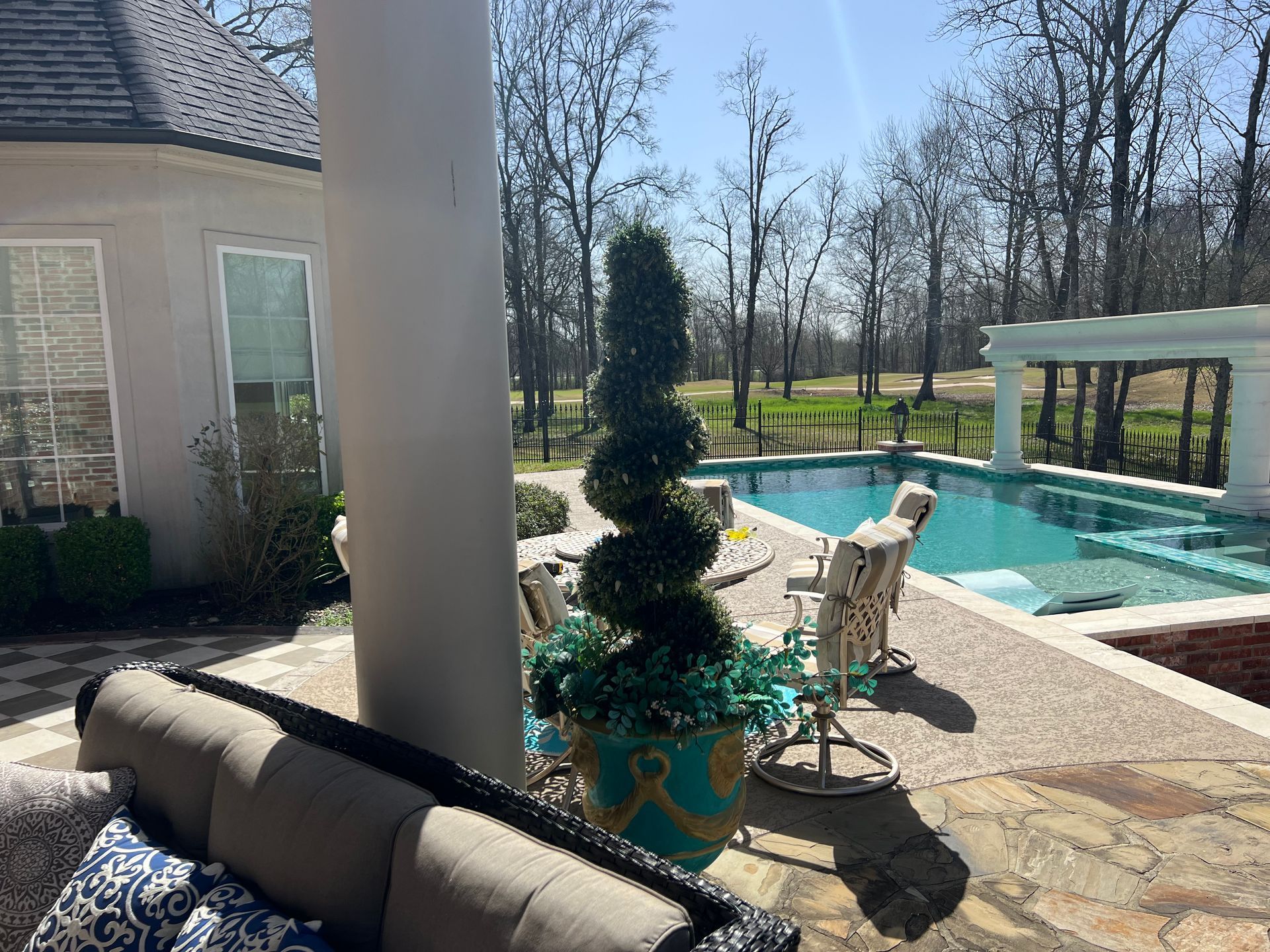 Patio with potted topiary beside a backyard pool and covered seating area