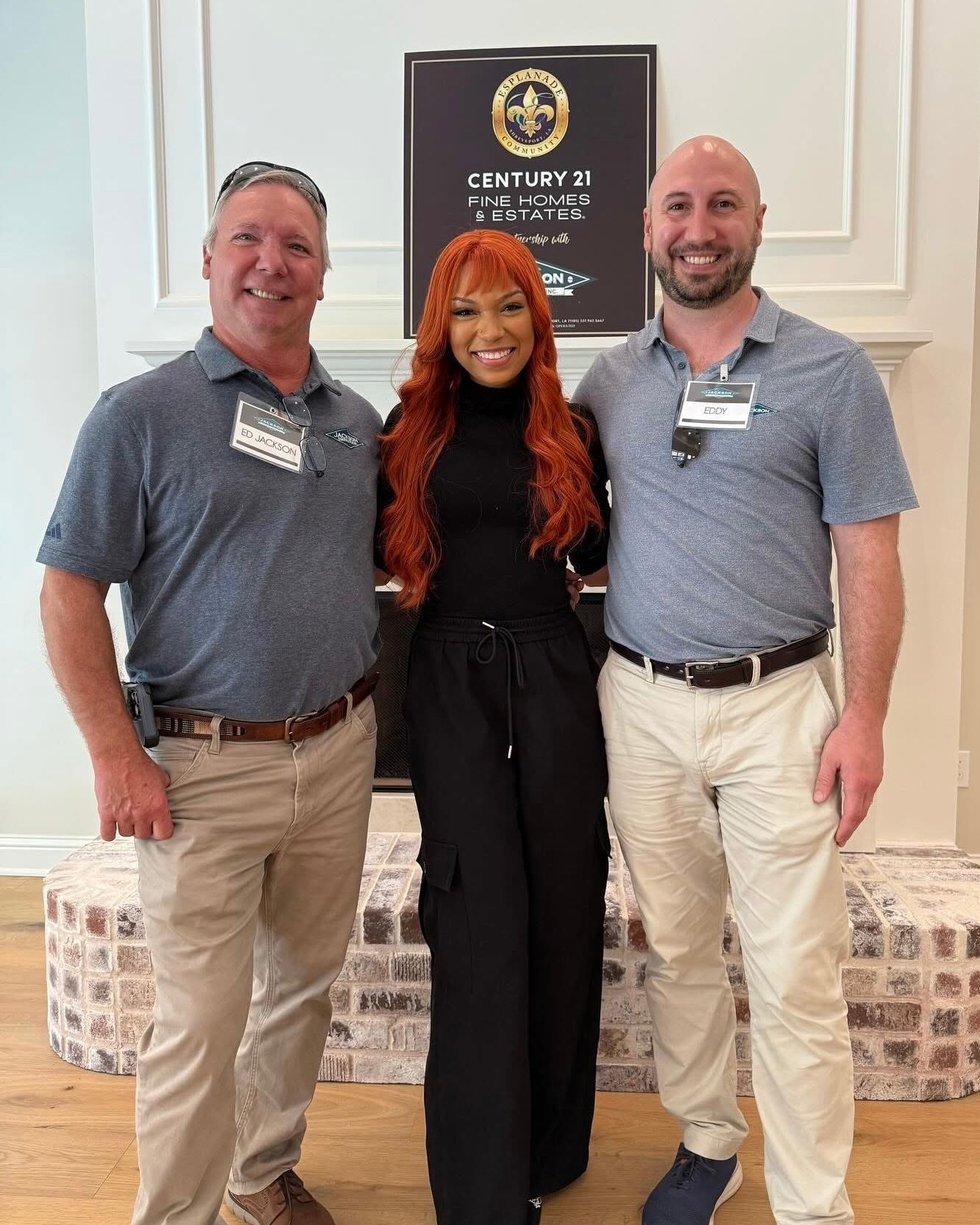 Three people posing indoors at an event, standing beside a black banner and smiling.