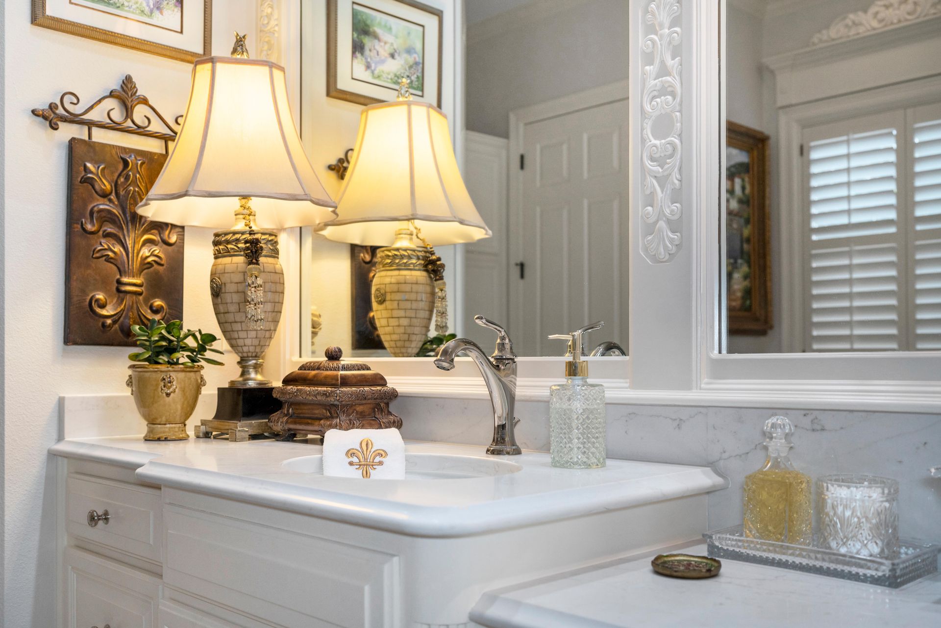 Elegant bathroom vanity with two lamps, ornate mirror, sink, and decorative bottles