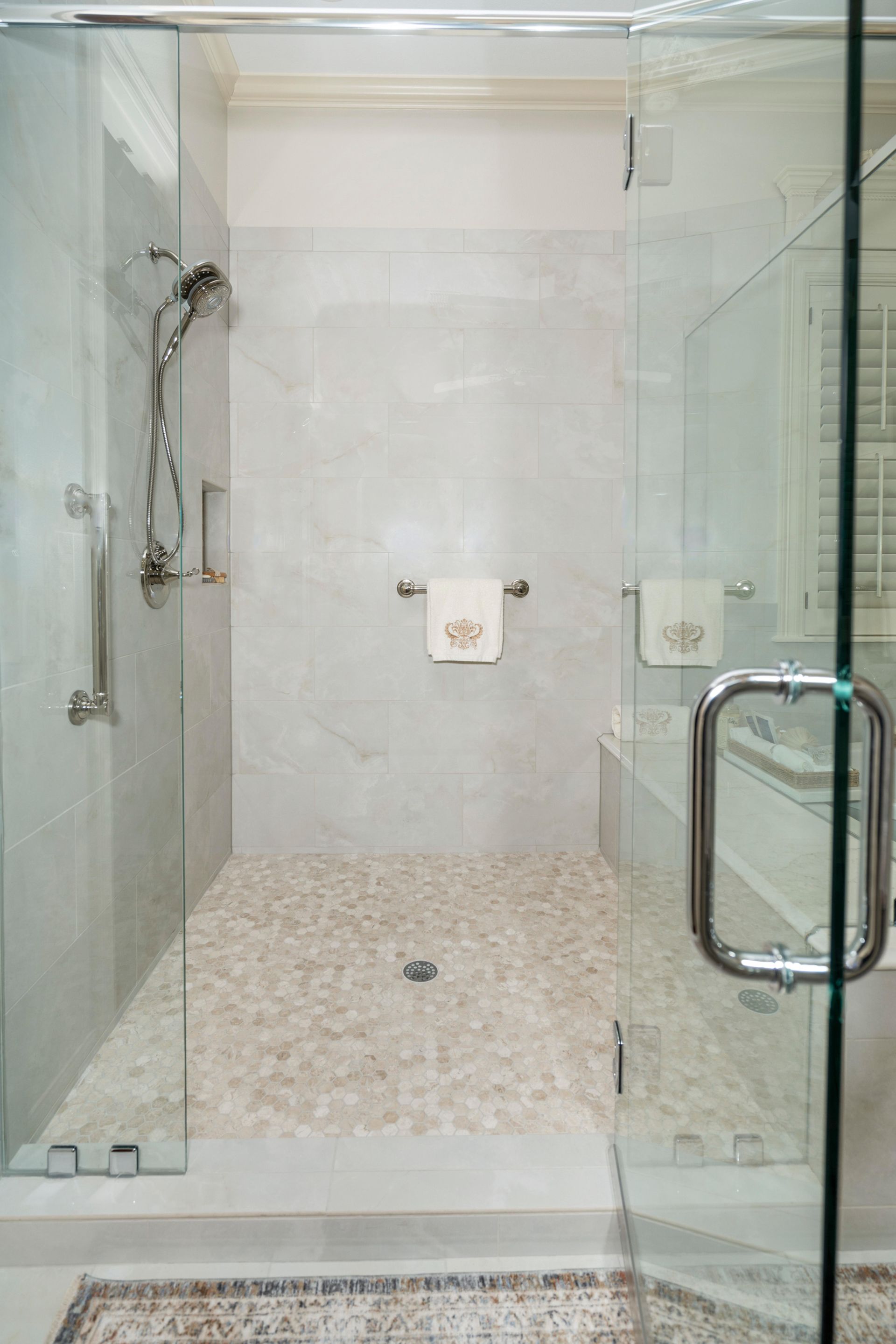 Glass-enclosed walk-in shower with tiled walls, handheld showerhead, and pebble-textured floor