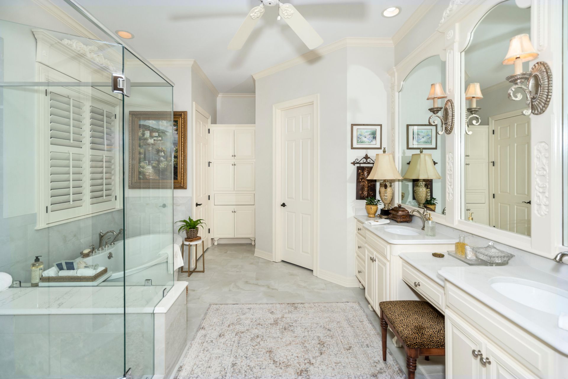 Bright white bathroom with glass shower, vanity, and mirrors, lit by chandeliers and natural light