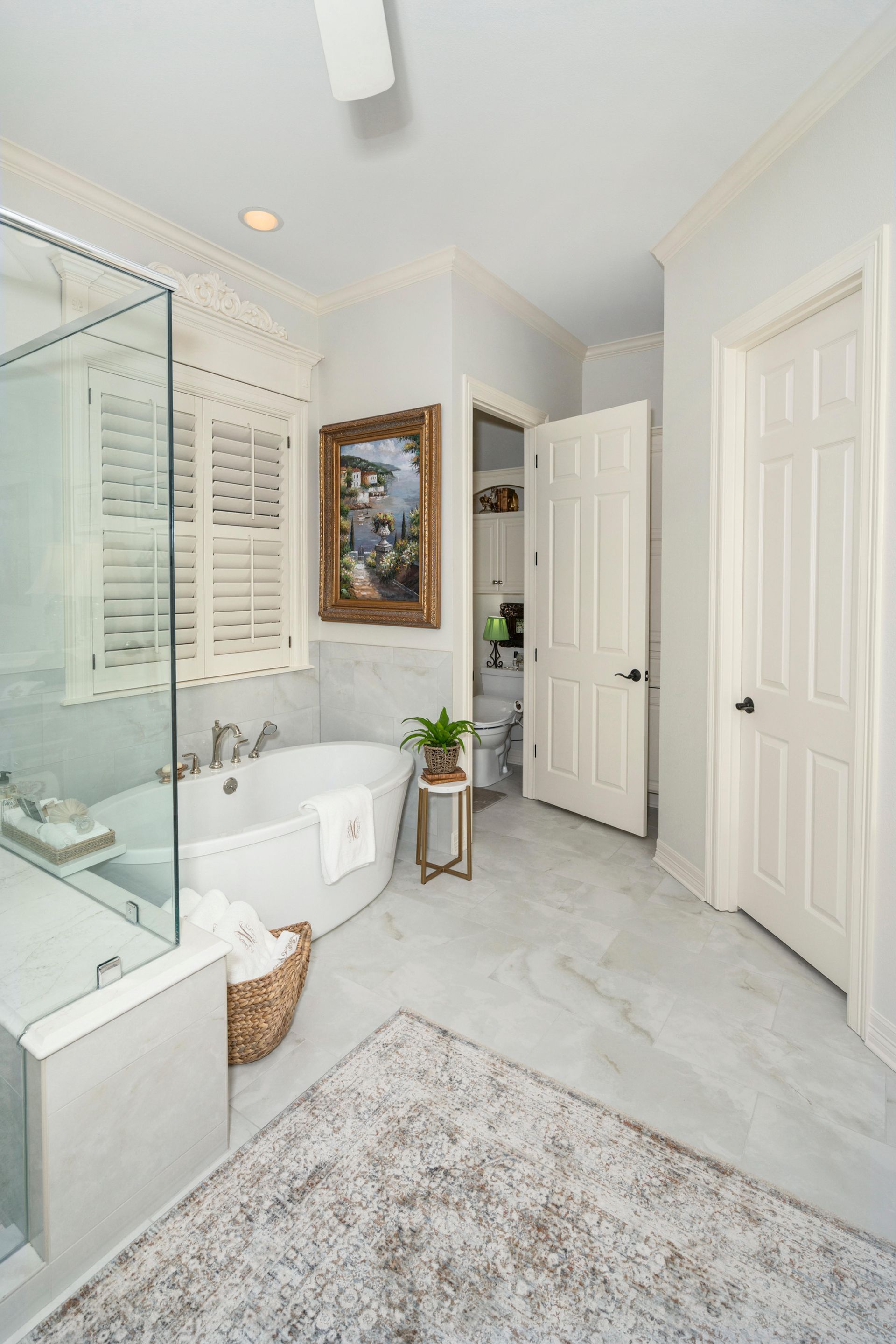 Bright white bathroom with glass shower, toilet, vanity, rug, and open door to a hallway