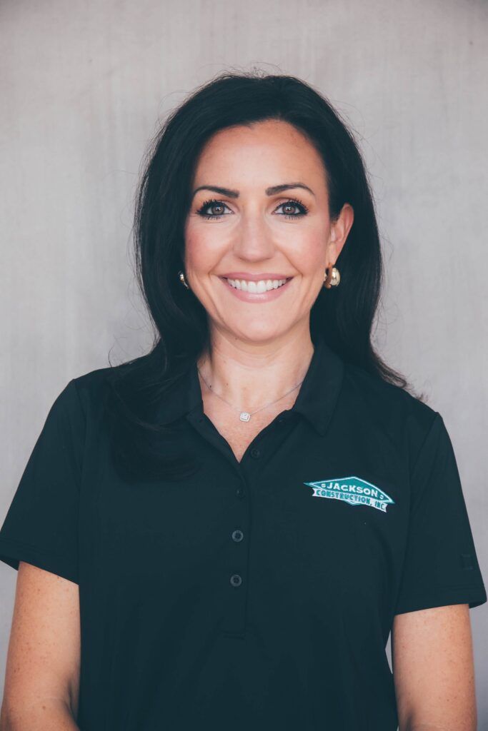 Smiling woman in a black polo shirt standing against a plain light background