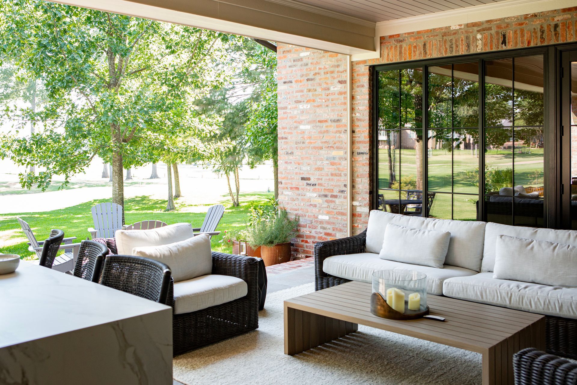 Modern patio with wicker sofas, coffee table, and garden view through large open windows.