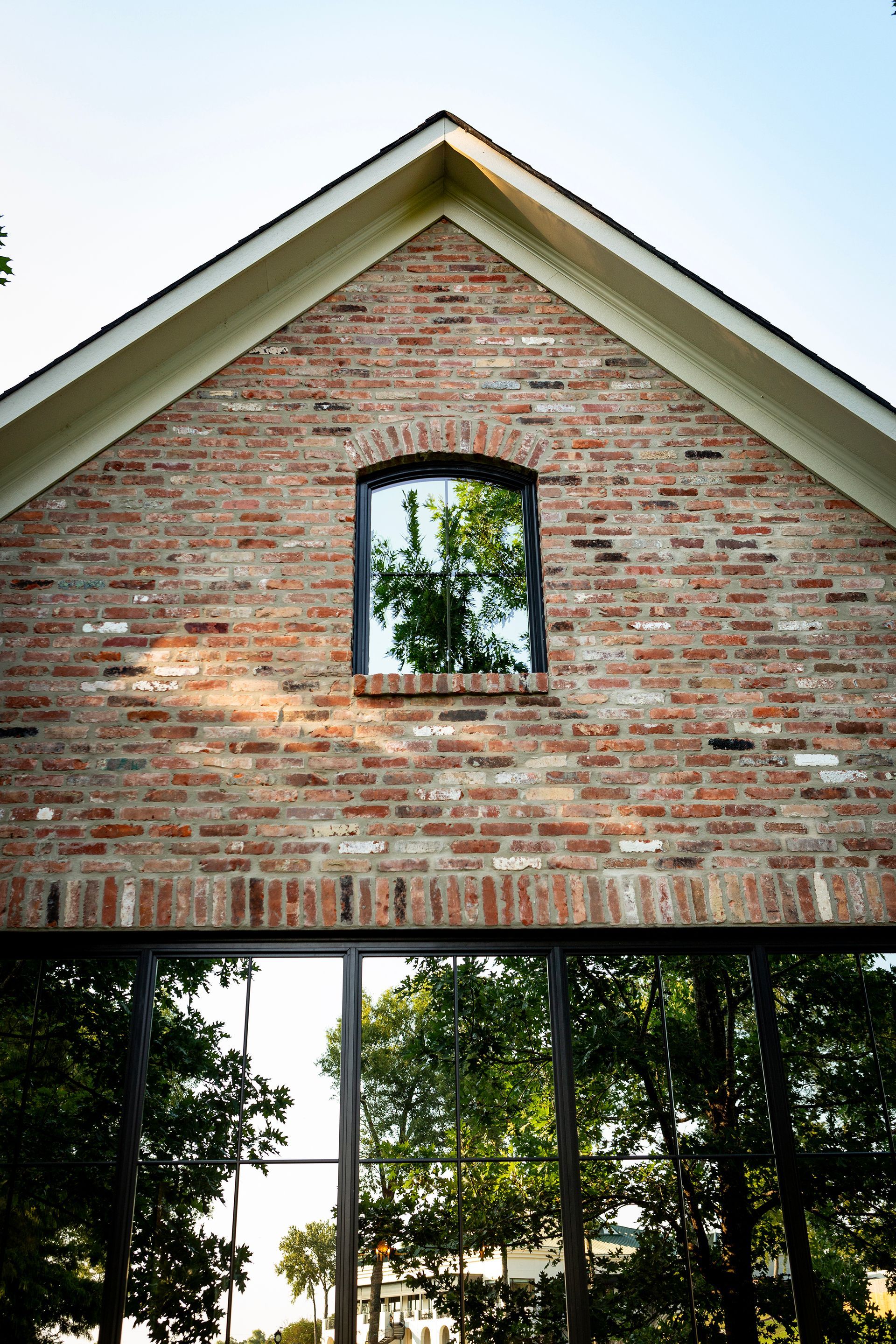 Brick house gable with small arched window above a view of trees and sky
