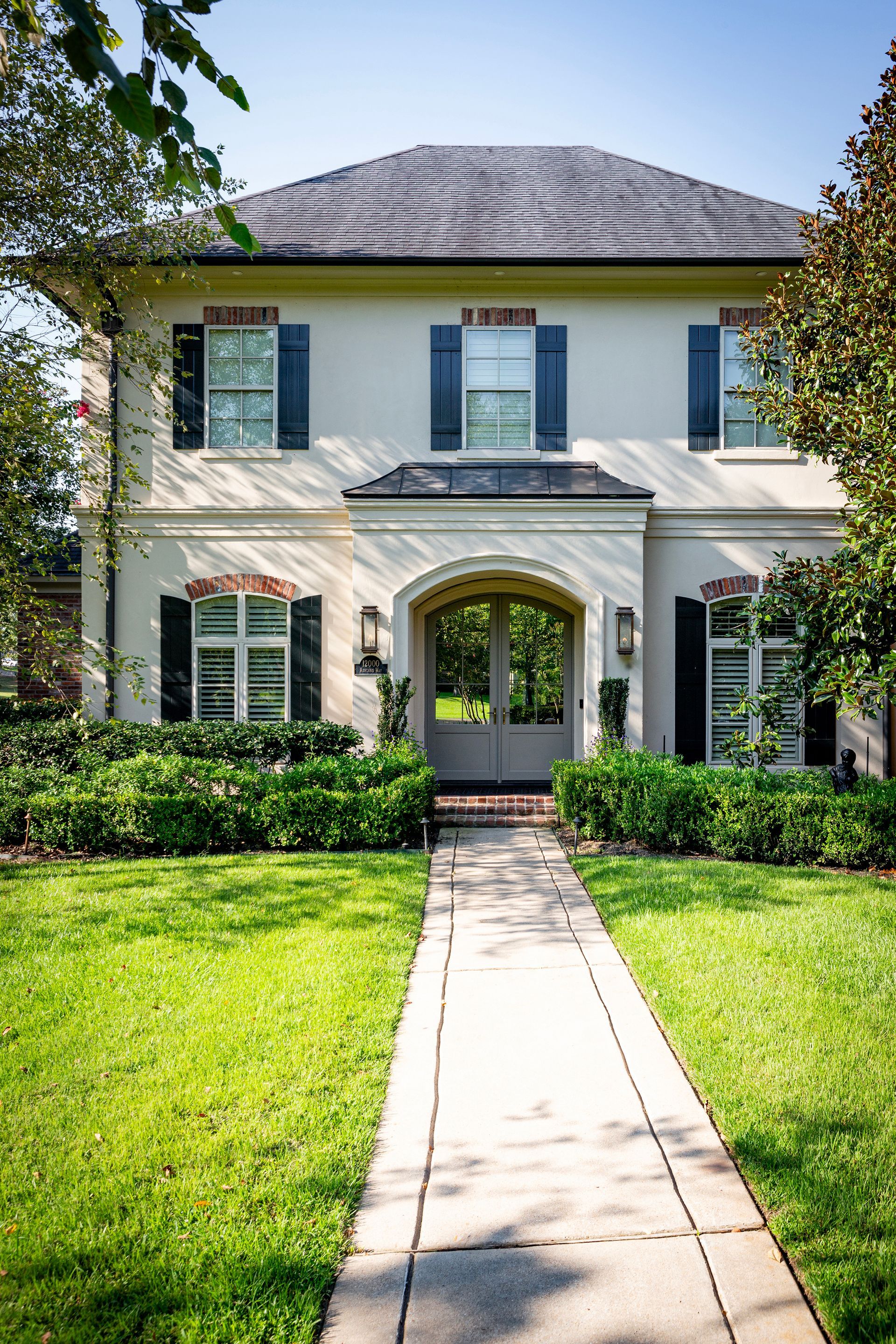 Front view of a white two-story house with blue shutters, an arched entryway, and a front walkway through a green lawn