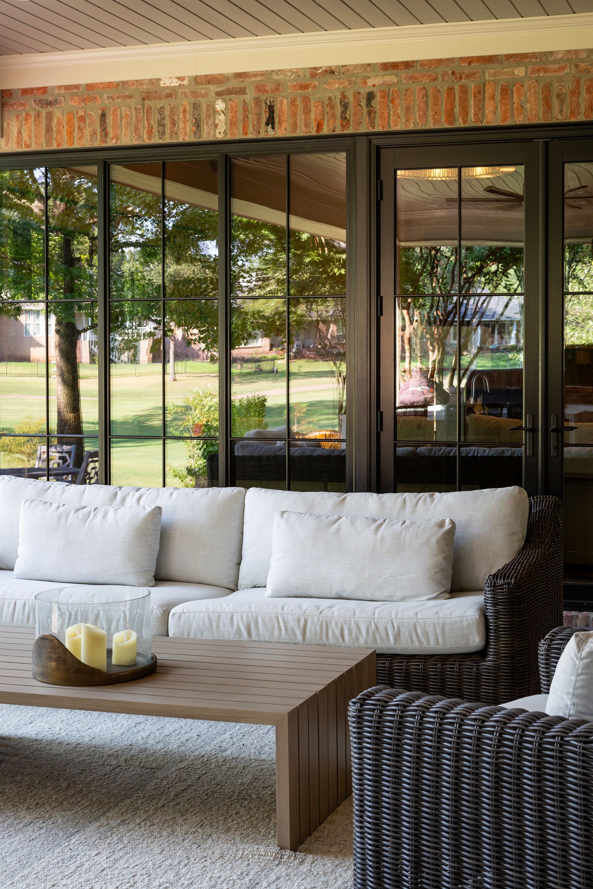 Patio seating with white cushions and wicker chair beside reflective glass walls and a wooden coffee table