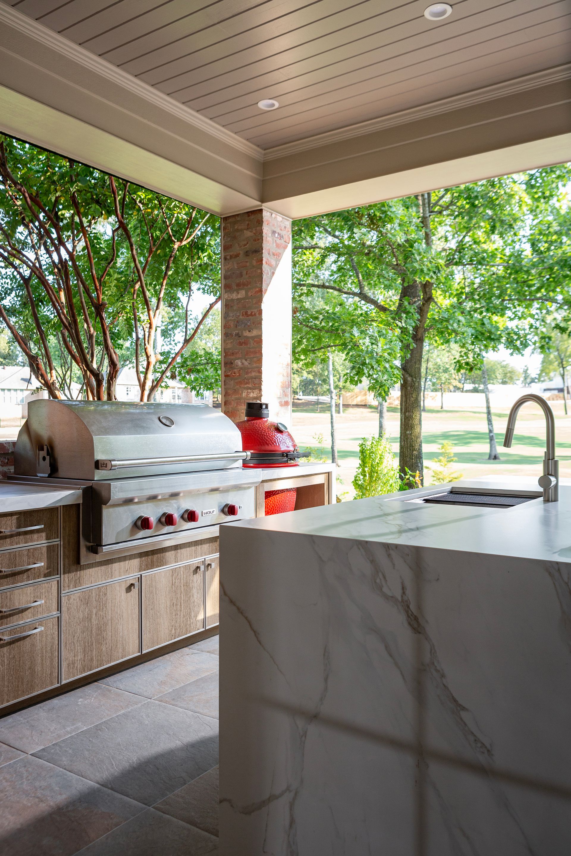 Outdoor kitchen with stainless grill, marble island, and trees in the background
