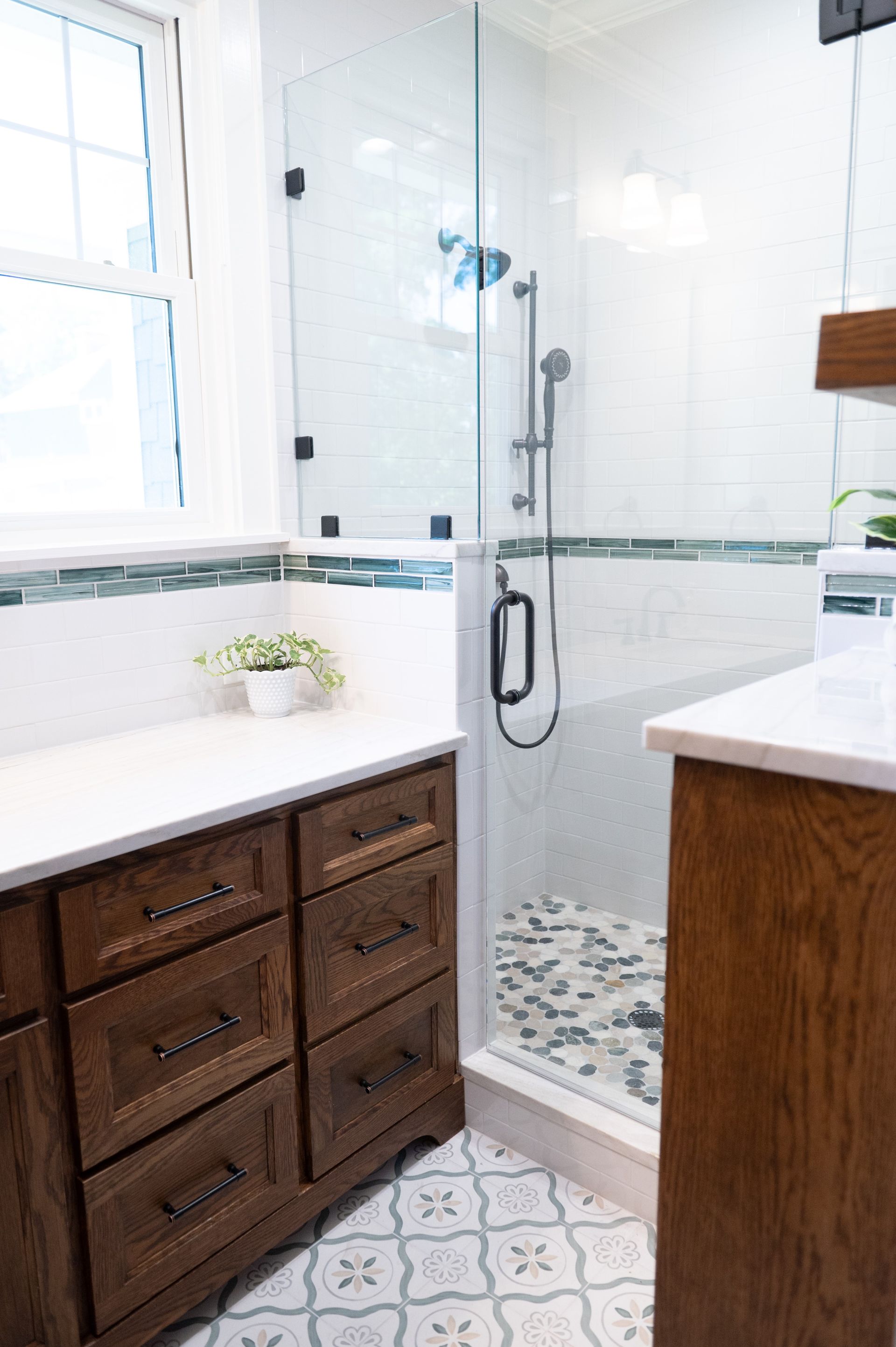 Bright bathroom with white tiled shower, dark wood vanity, and patterned floor tiles.