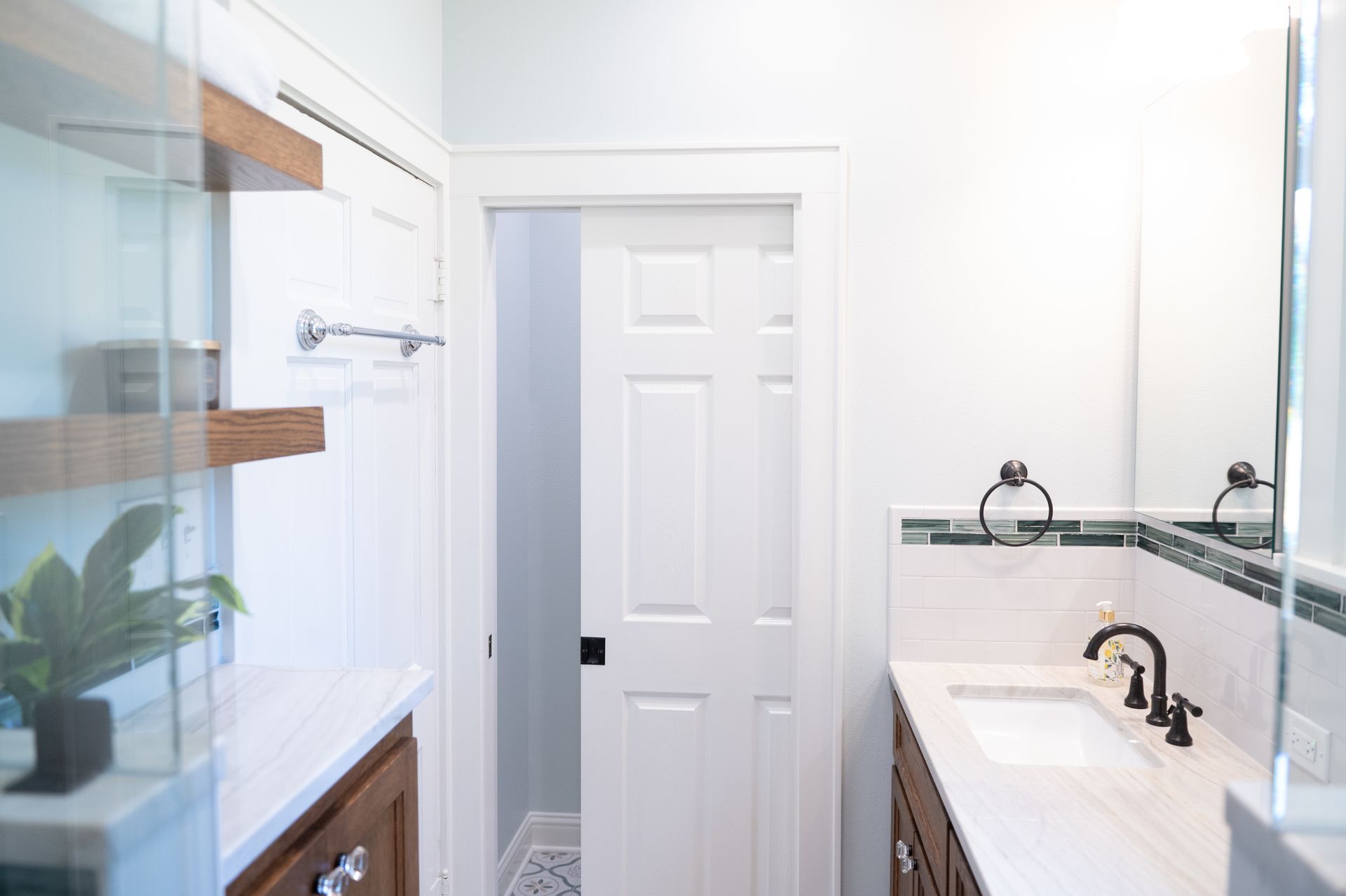 Bright bathroom with glass shower, white vanity, black fixtures, and a closed door at the back.
