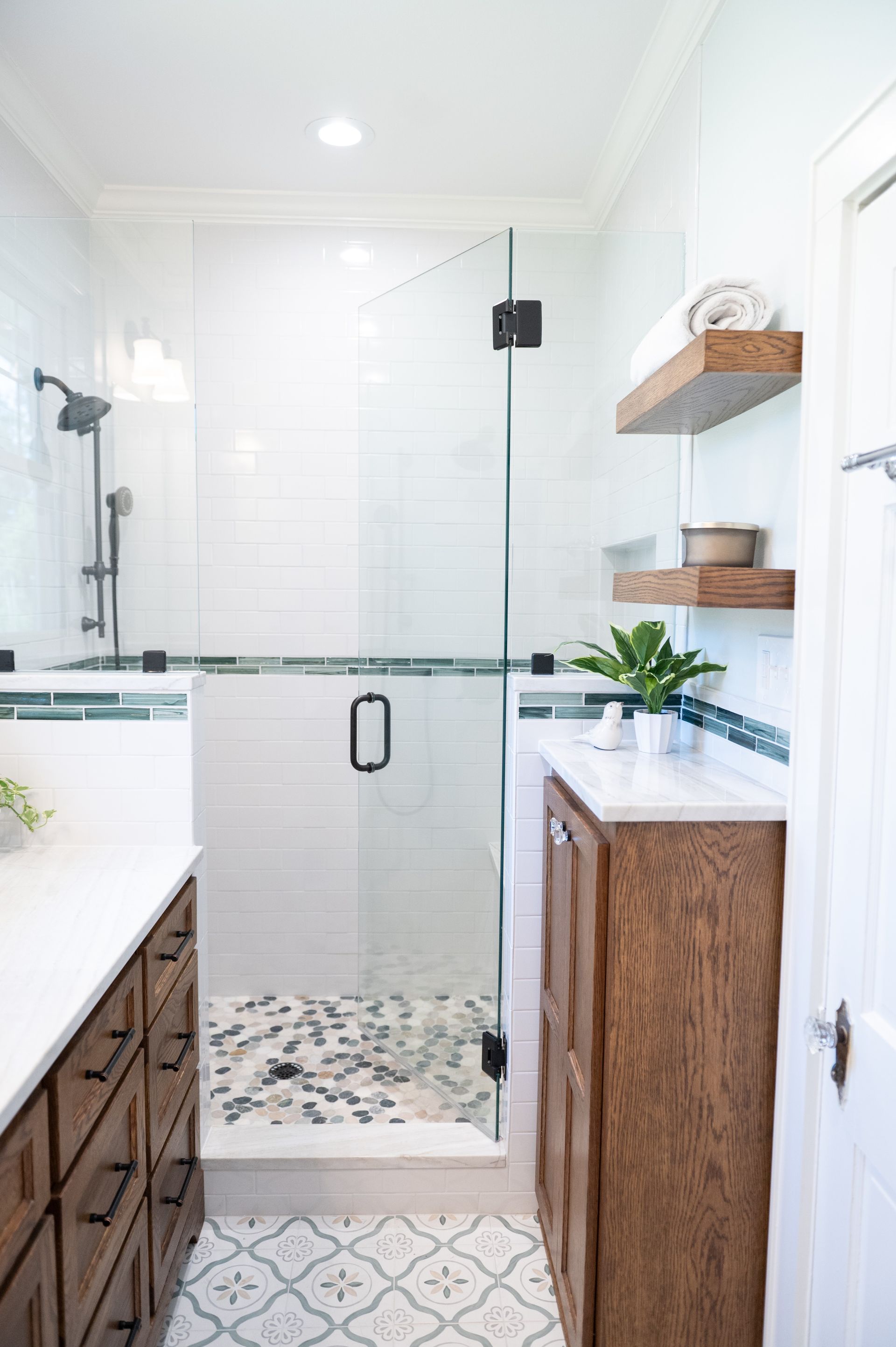 Bright modern bathroom with a glass shower, white tile, wood vanities, and a woven stool.