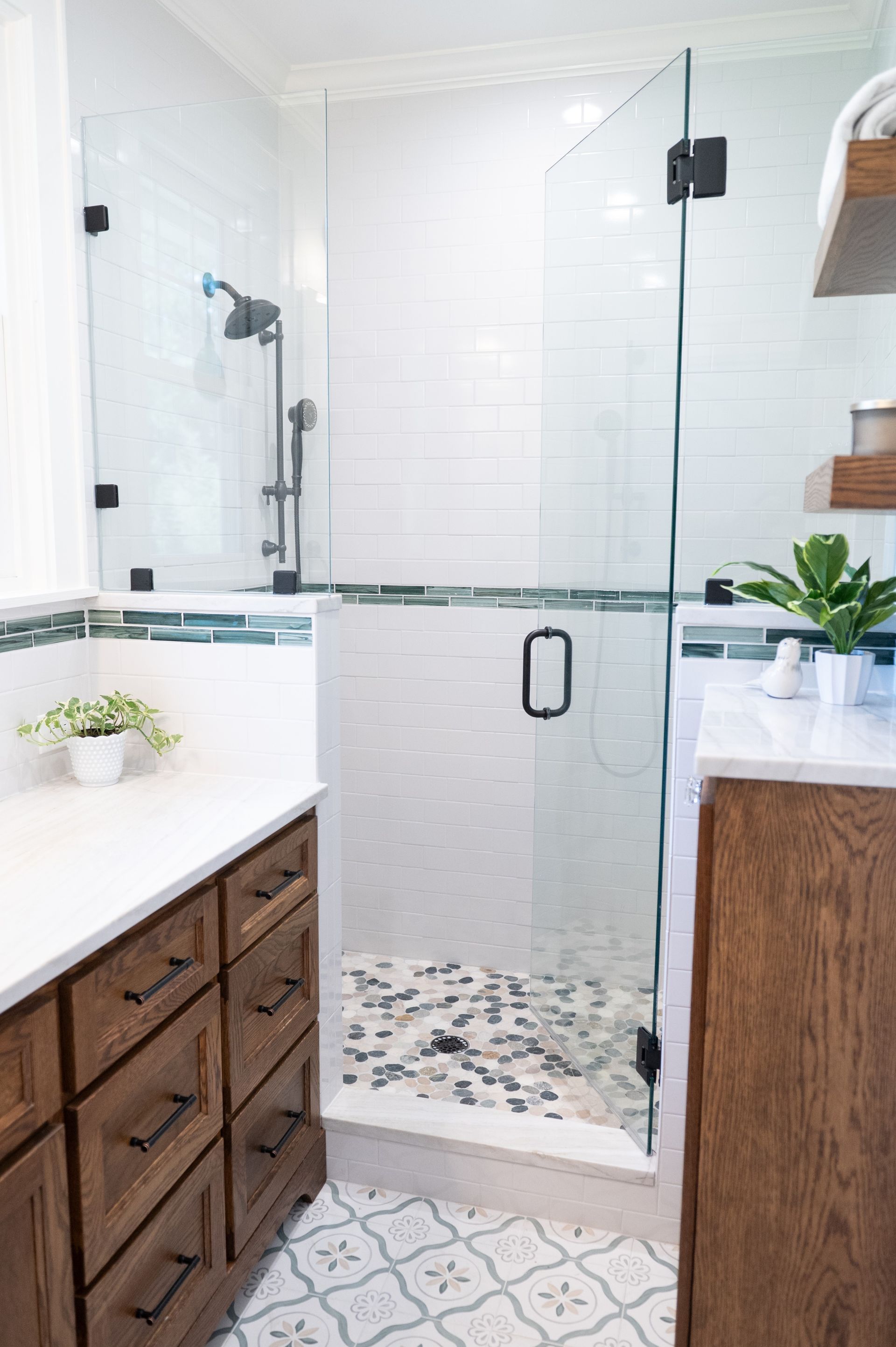 Modern white bathroom with glass shower, patterned tile floor, and wood vanity cabinets