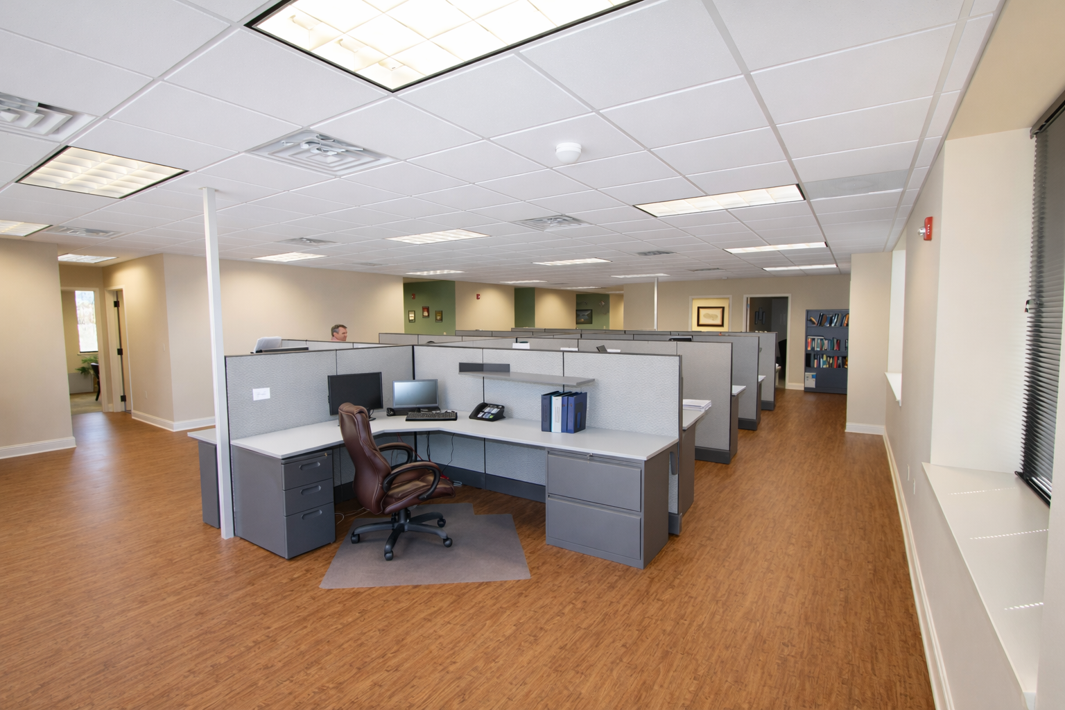 Open-plan office with cubicles, chairs, desks, and overhead fluorescent lighting