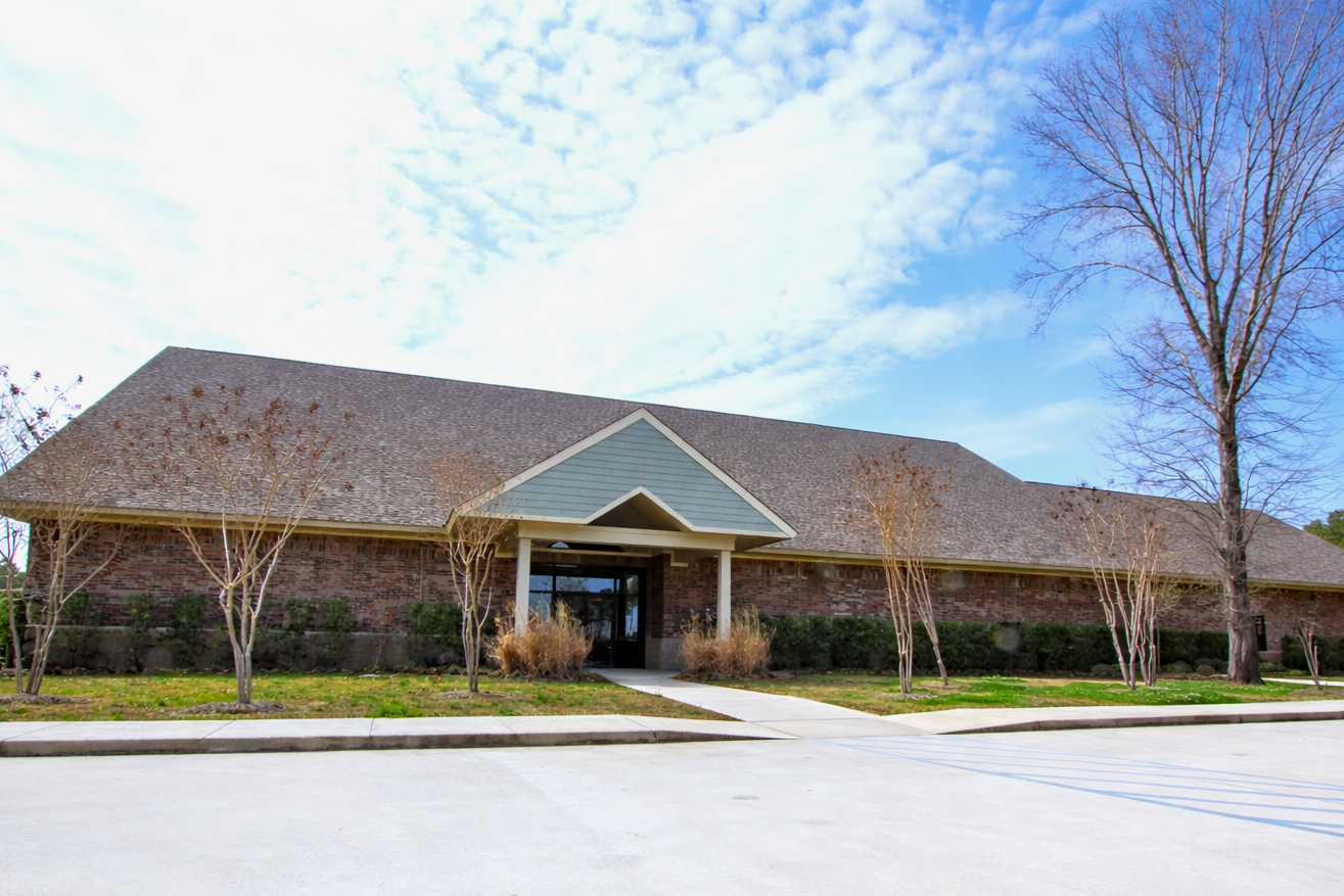 Single-story building with a peaked entrance, brick exterior, and bare trees under a bright blue sky