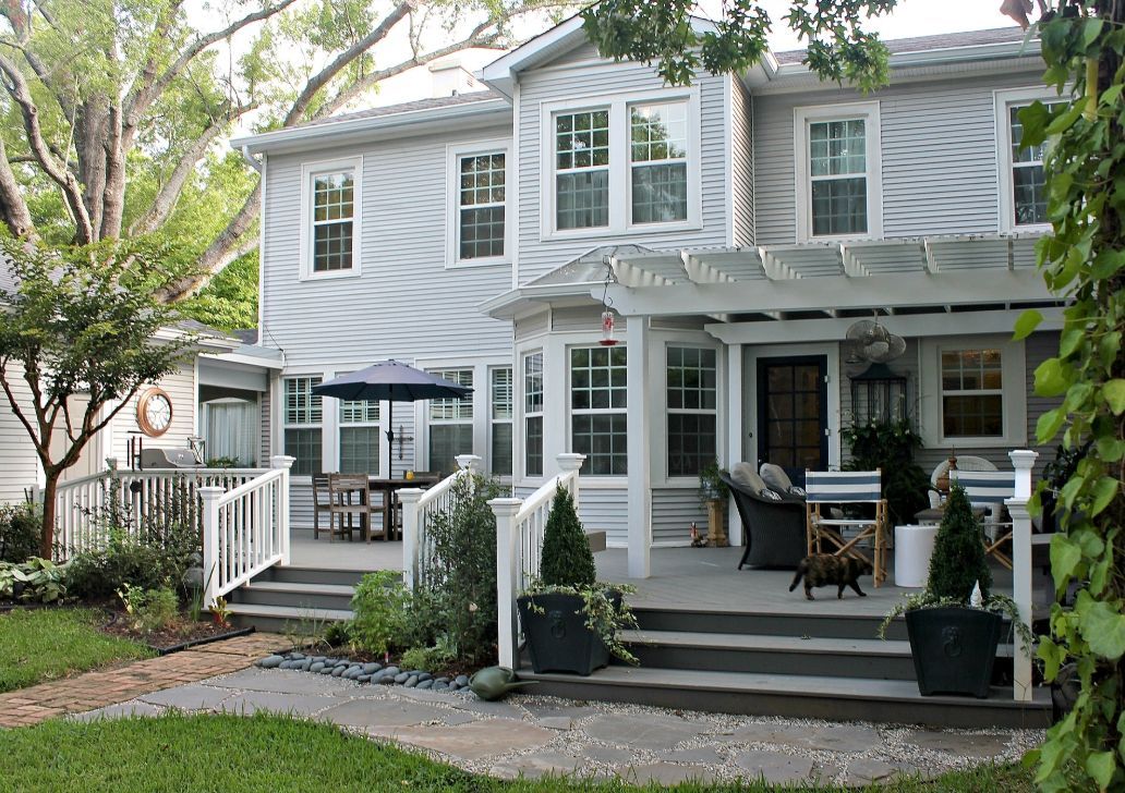 Gray two-story house with white trim, front porch, and a small lawn under leafy trees