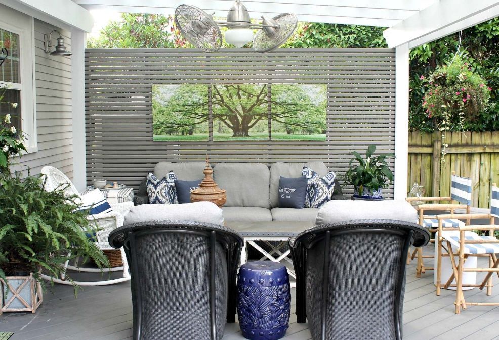 Patio seating area with wicker chairs, gray sofa, and garden view under a covered pergola