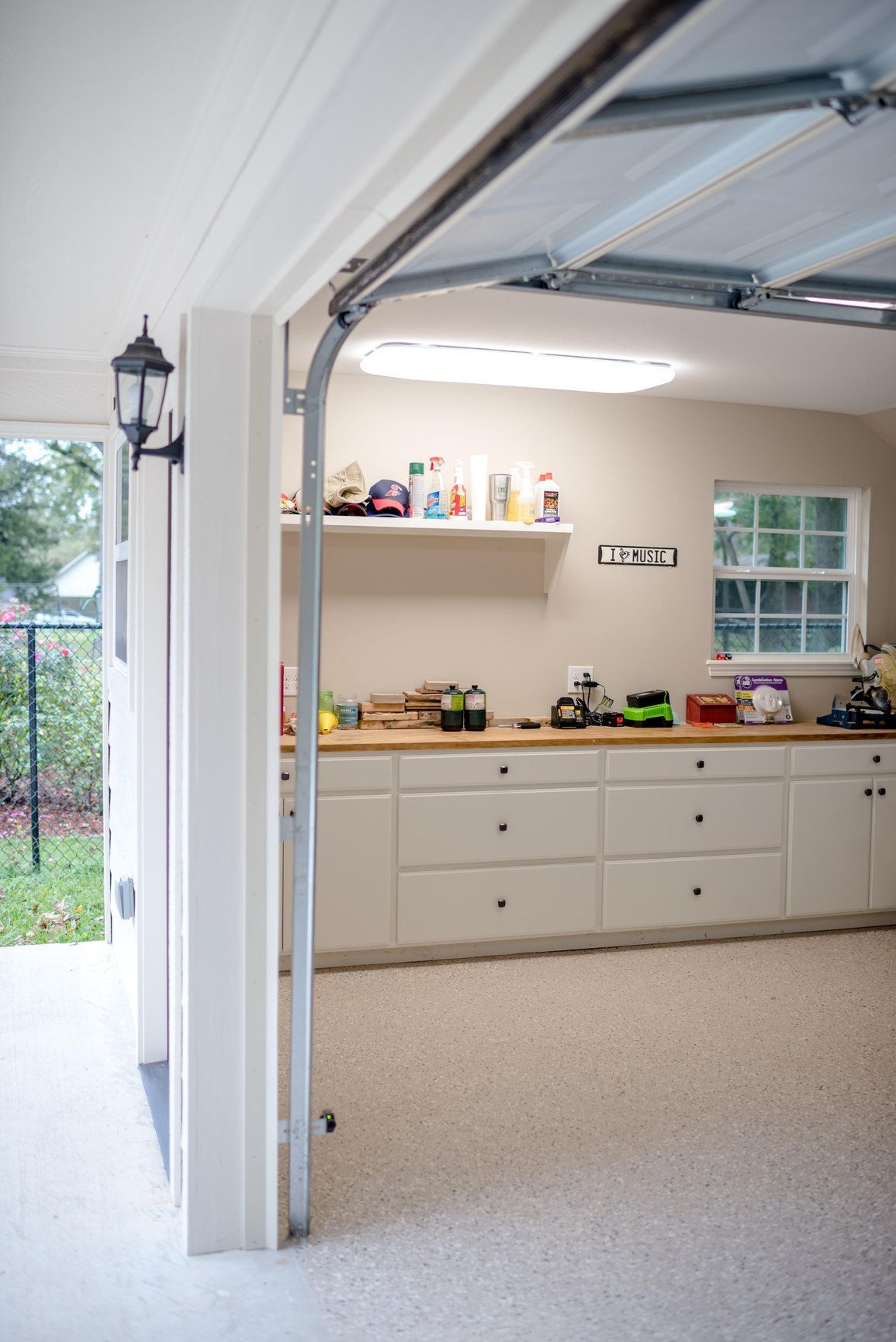 Open garage view of a white workshop with cabinets, tools, shelves, and a window.