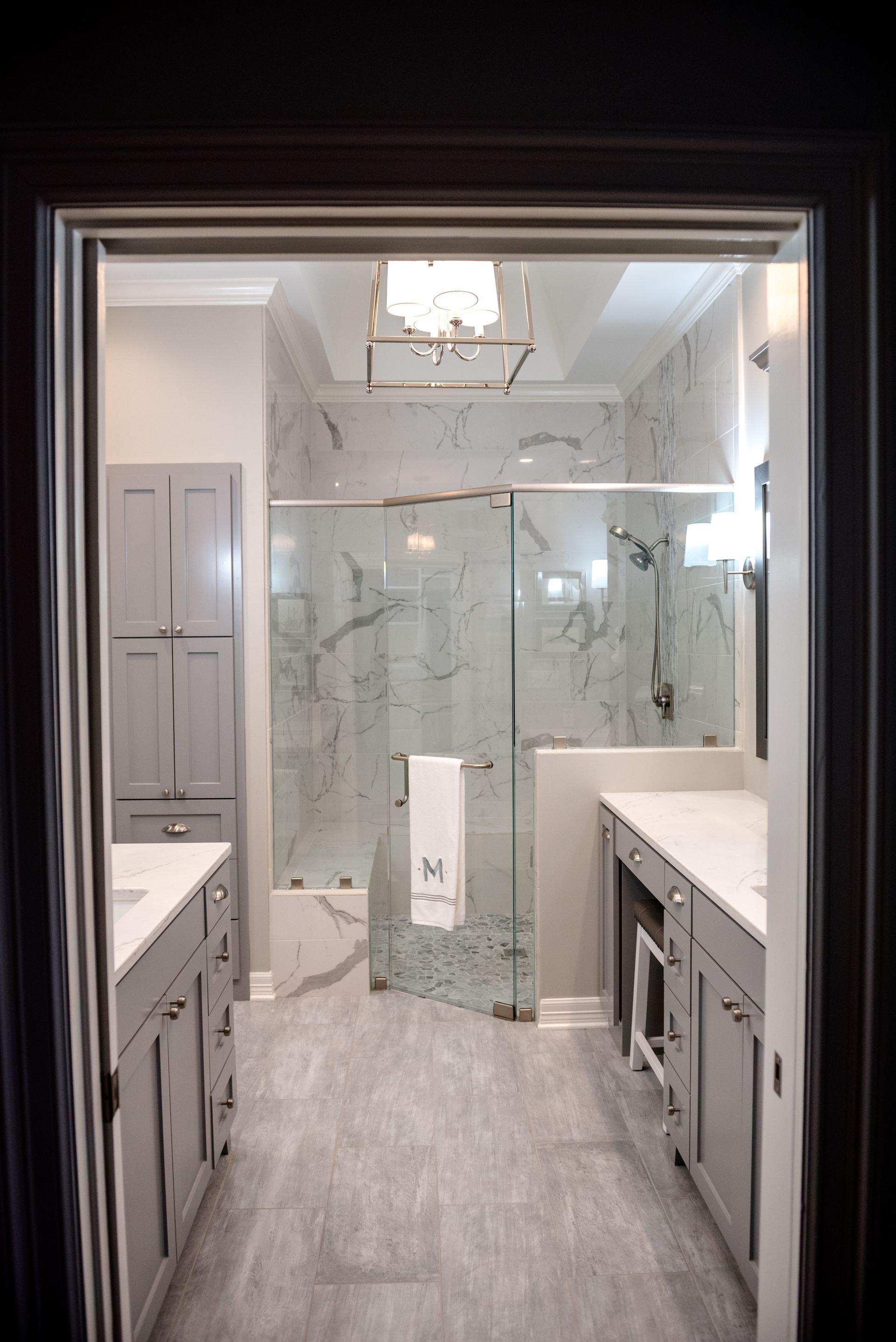Bright modern bathroom with marble shower, double vanity, and gray tile floor