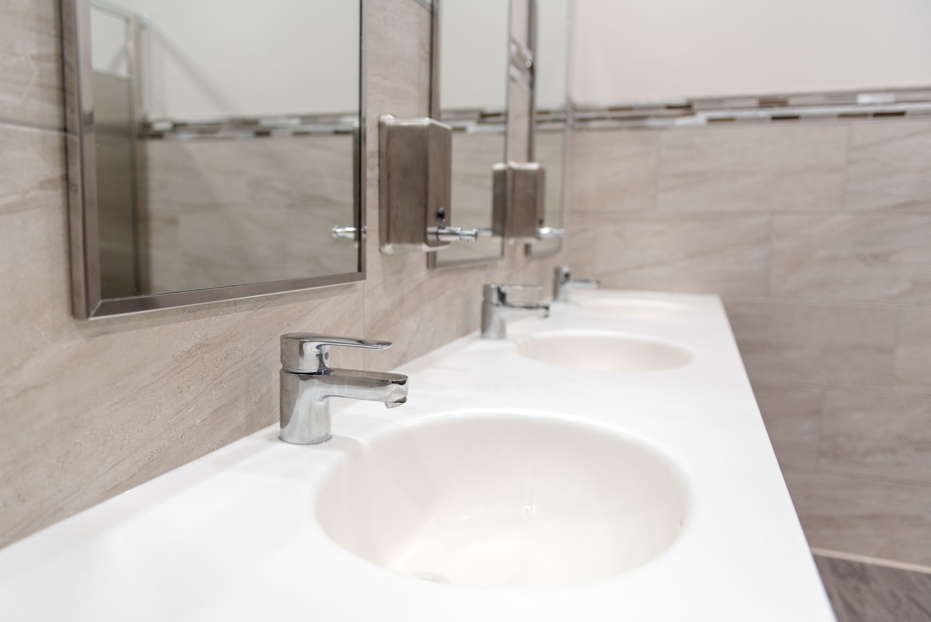 Public restroom sink with chrome faucets and mirrors above a white countertop.