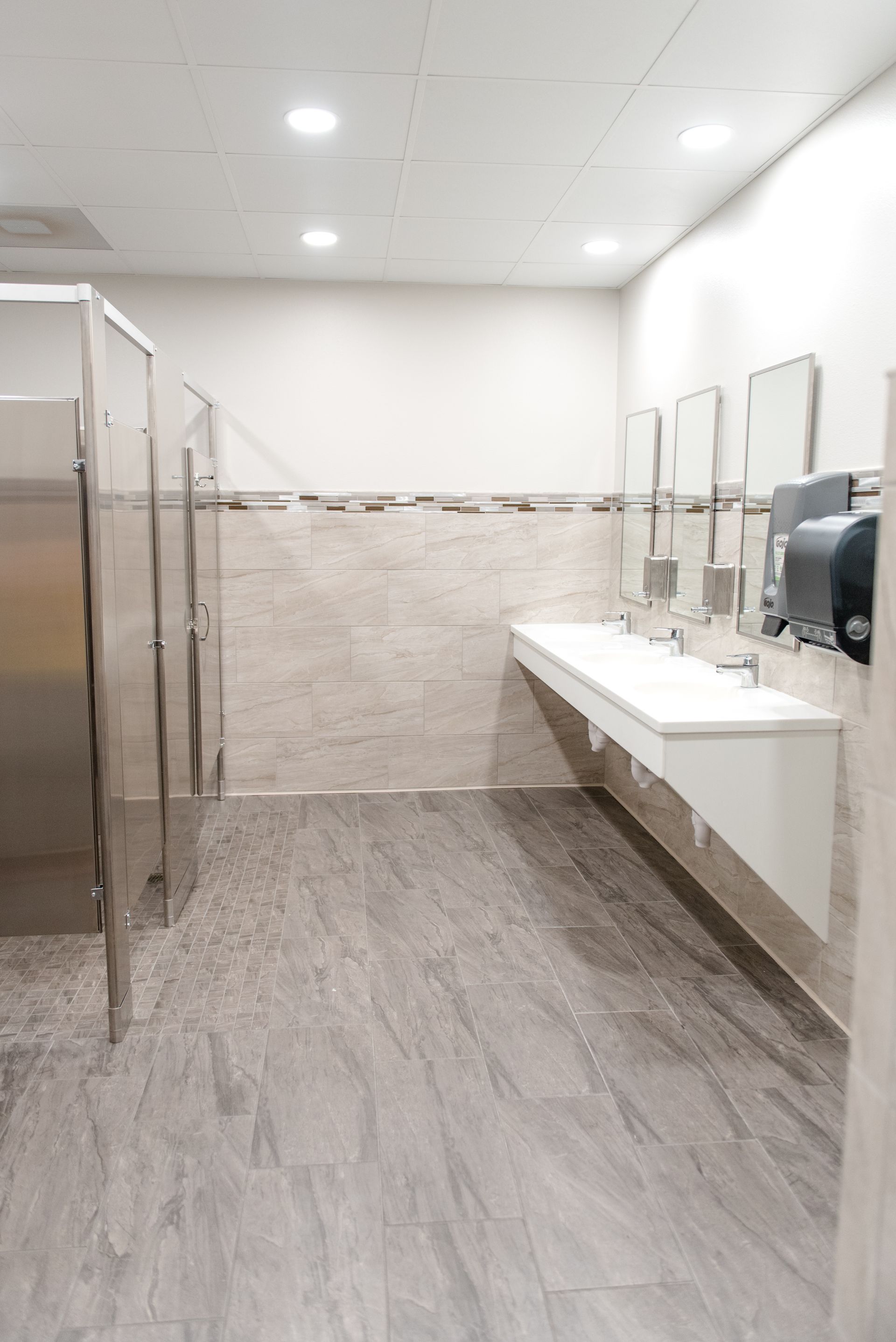 Empty modern restroom with sinks, mirrors, tiled walls, and gray flooring