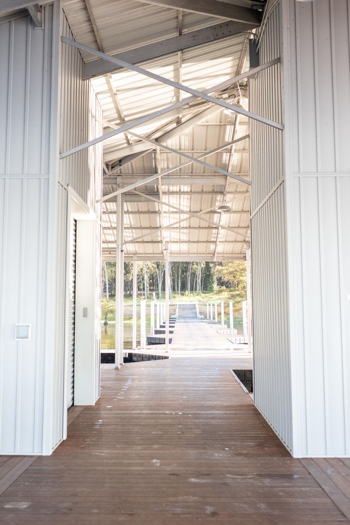 Covered wooden walkway with white metal walls and roof, leading toward a bright outdoor view.