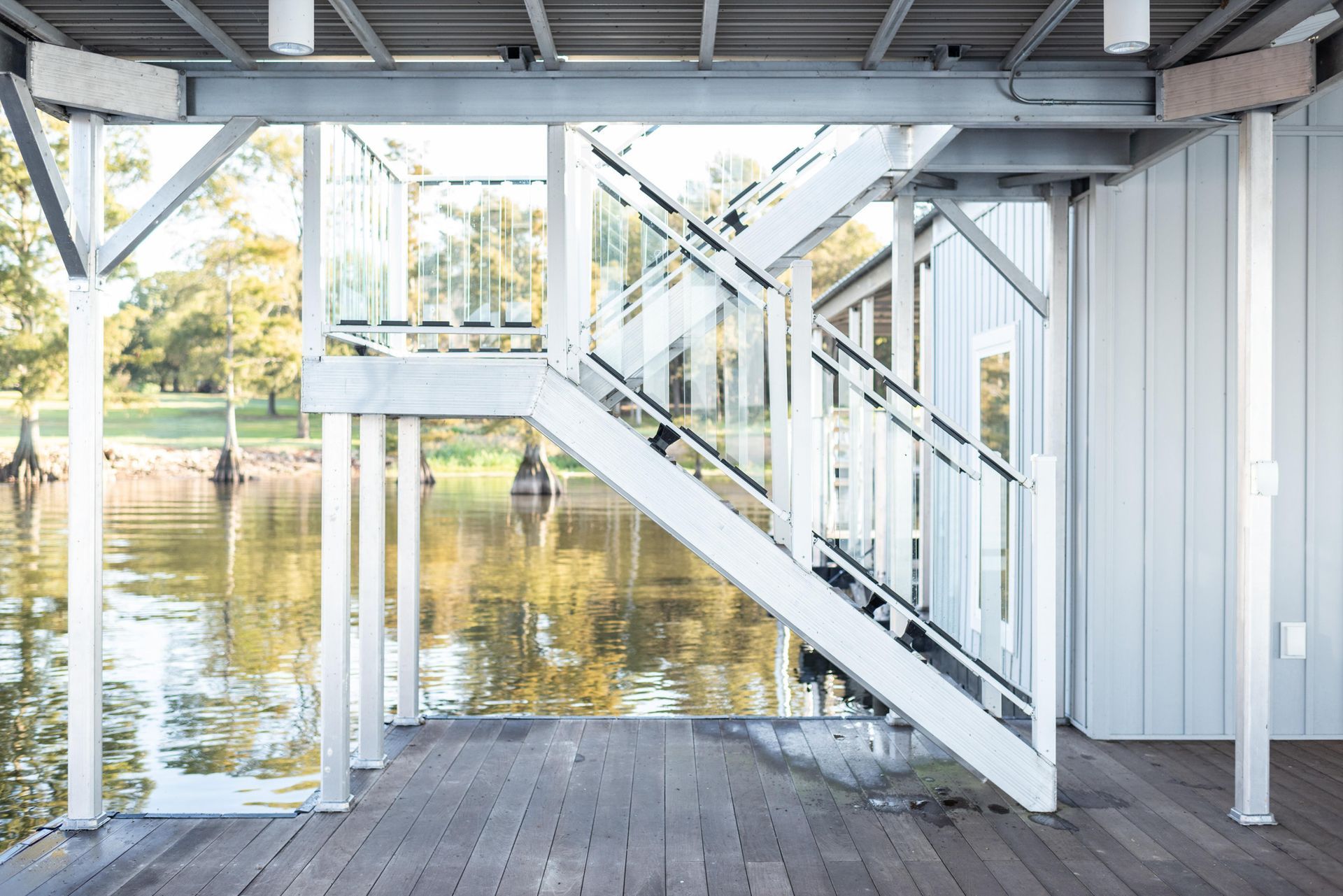 Covered wooden deck with white stairs and railings overlooking a calm lake