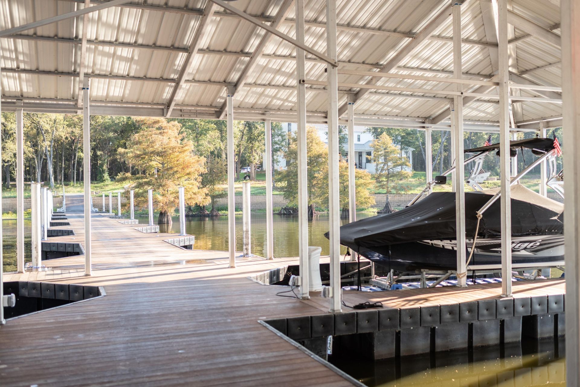 Covered wooden dock with white metal roof, open water, and a black boat under repair beside the walkway