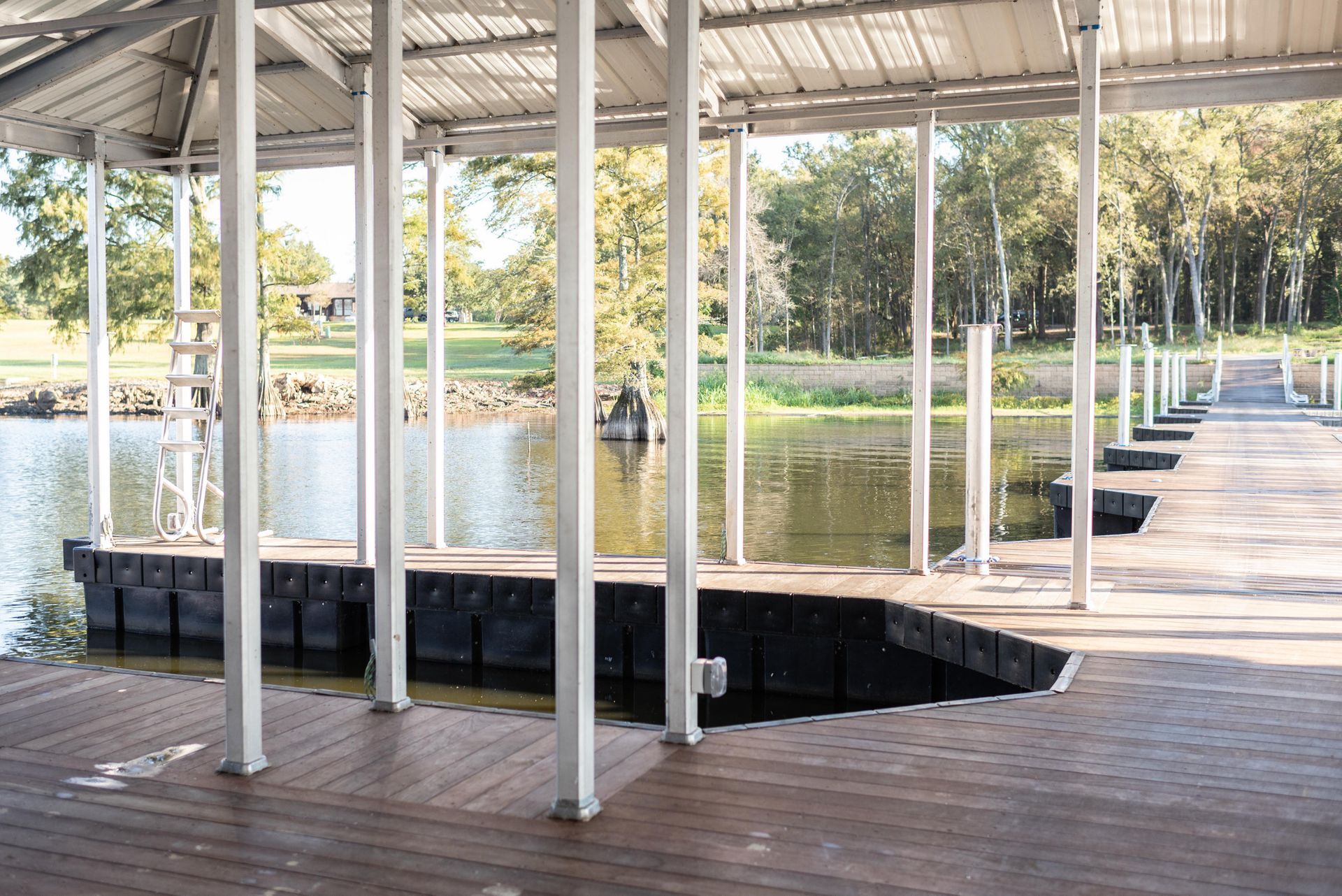 Open-air pavilion with white columns beside a pond and brick walkway, lit by sunlight