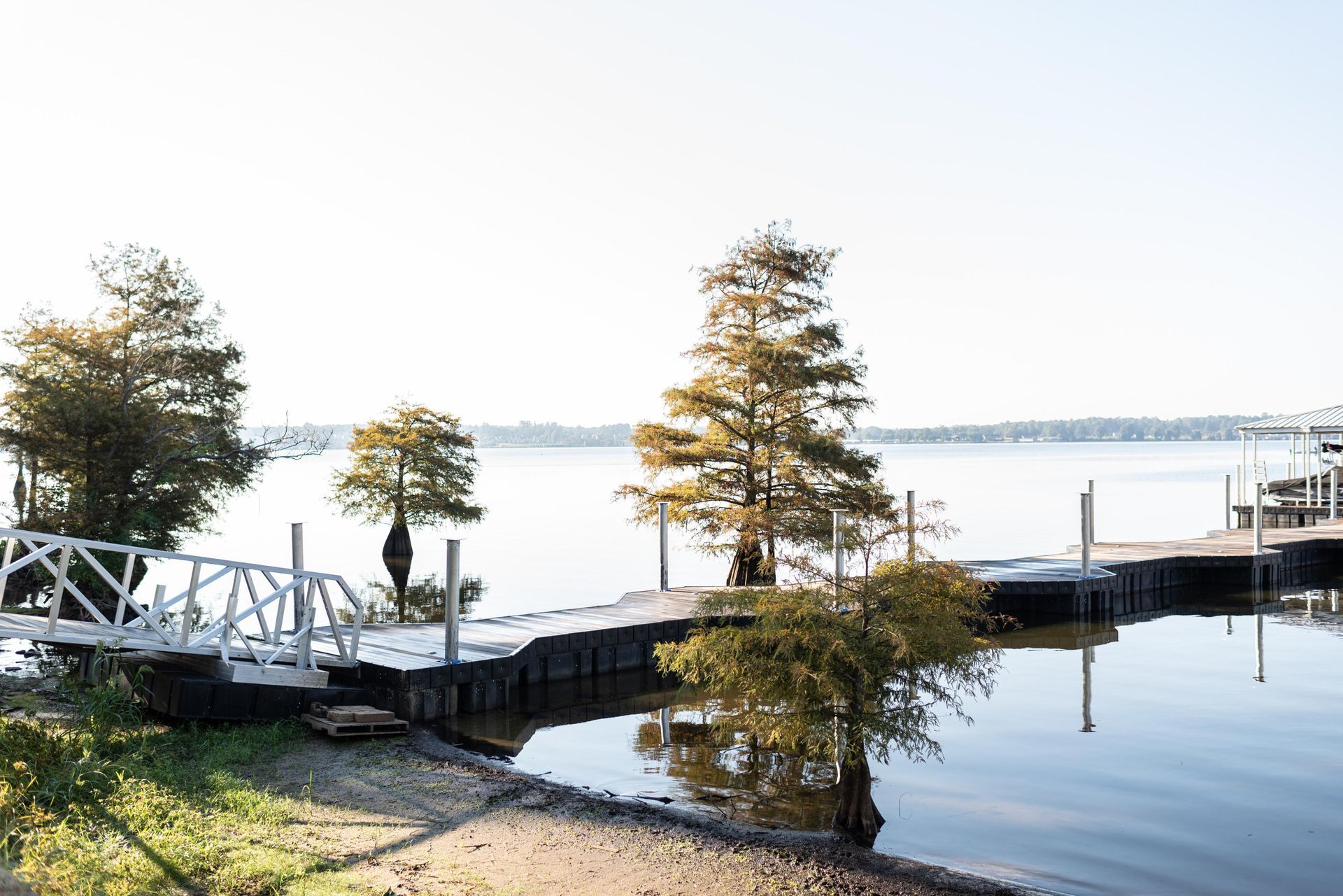 Calm waterfront with dock, small bridge, trees, and reflections on still water under a clear sky