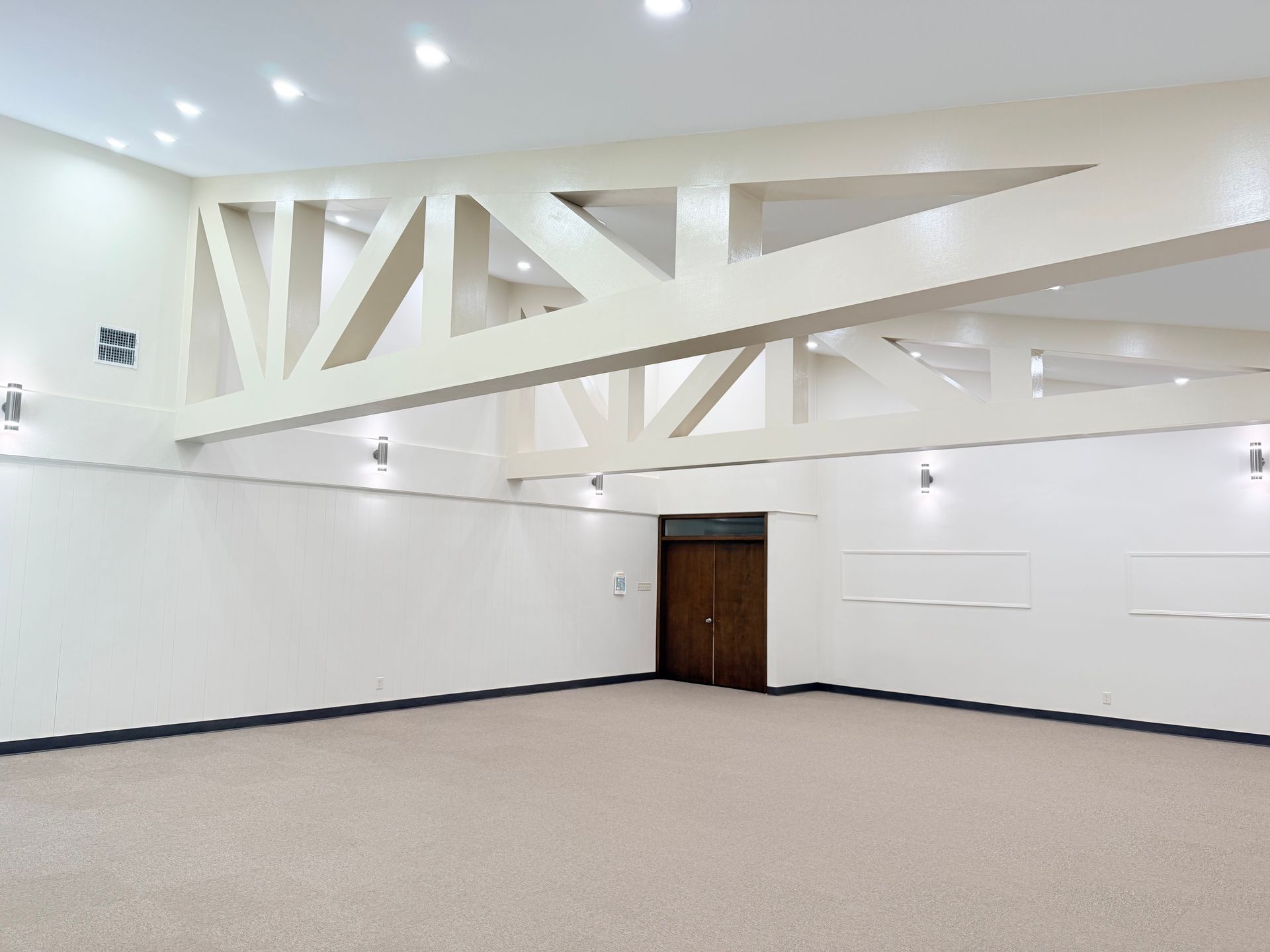 Empty modern room with white walls, exposed beams, and a single wooden door