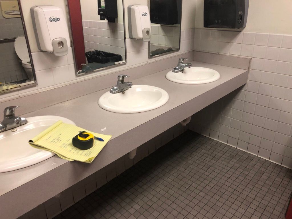 Public restroom sinks with mirrors, soap dispensers, and a yellow cleaning cloth on the counter.