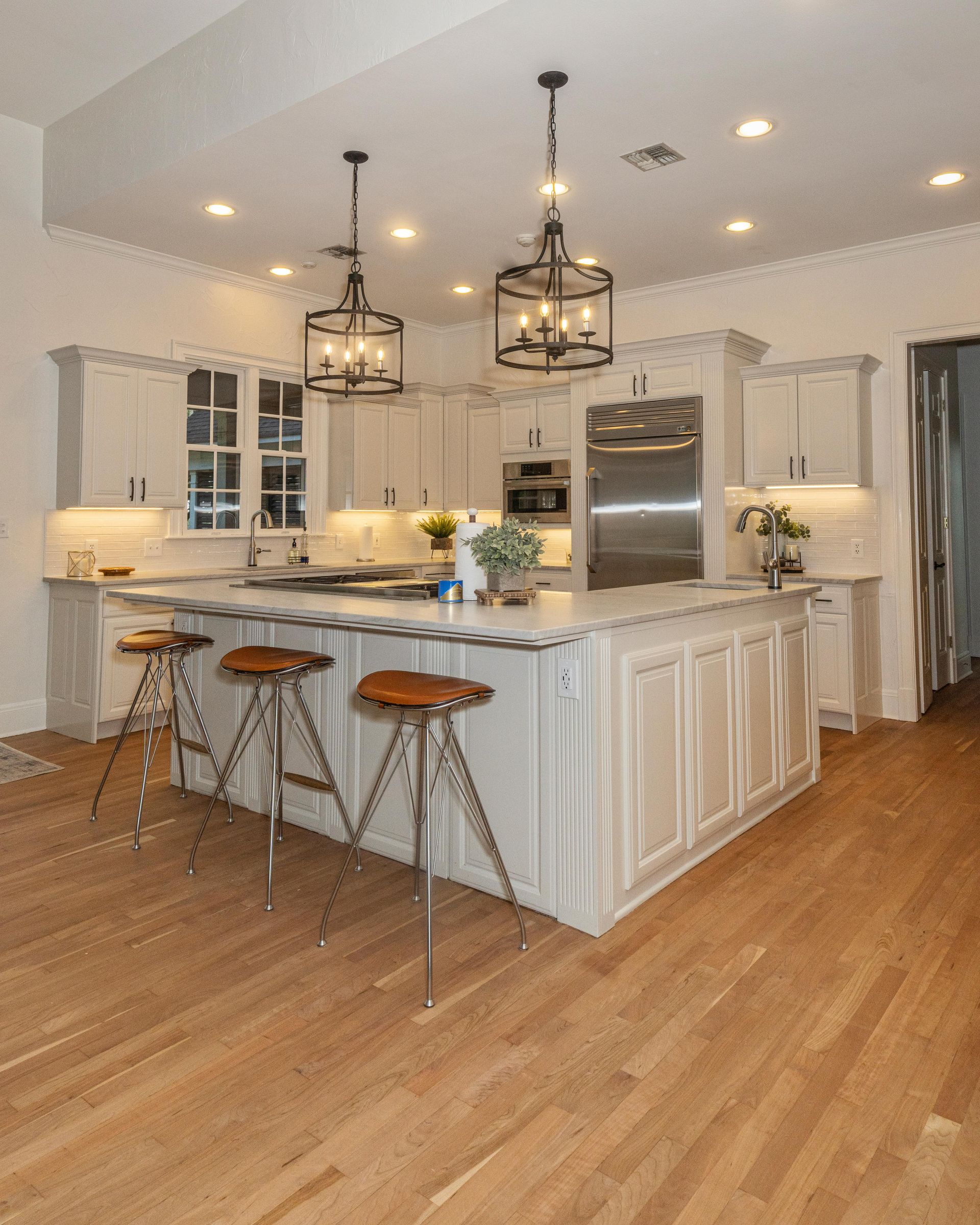 Bright modern kitchen with white cabinets, marble island, bar stools, pendant lights, and hardwood floor