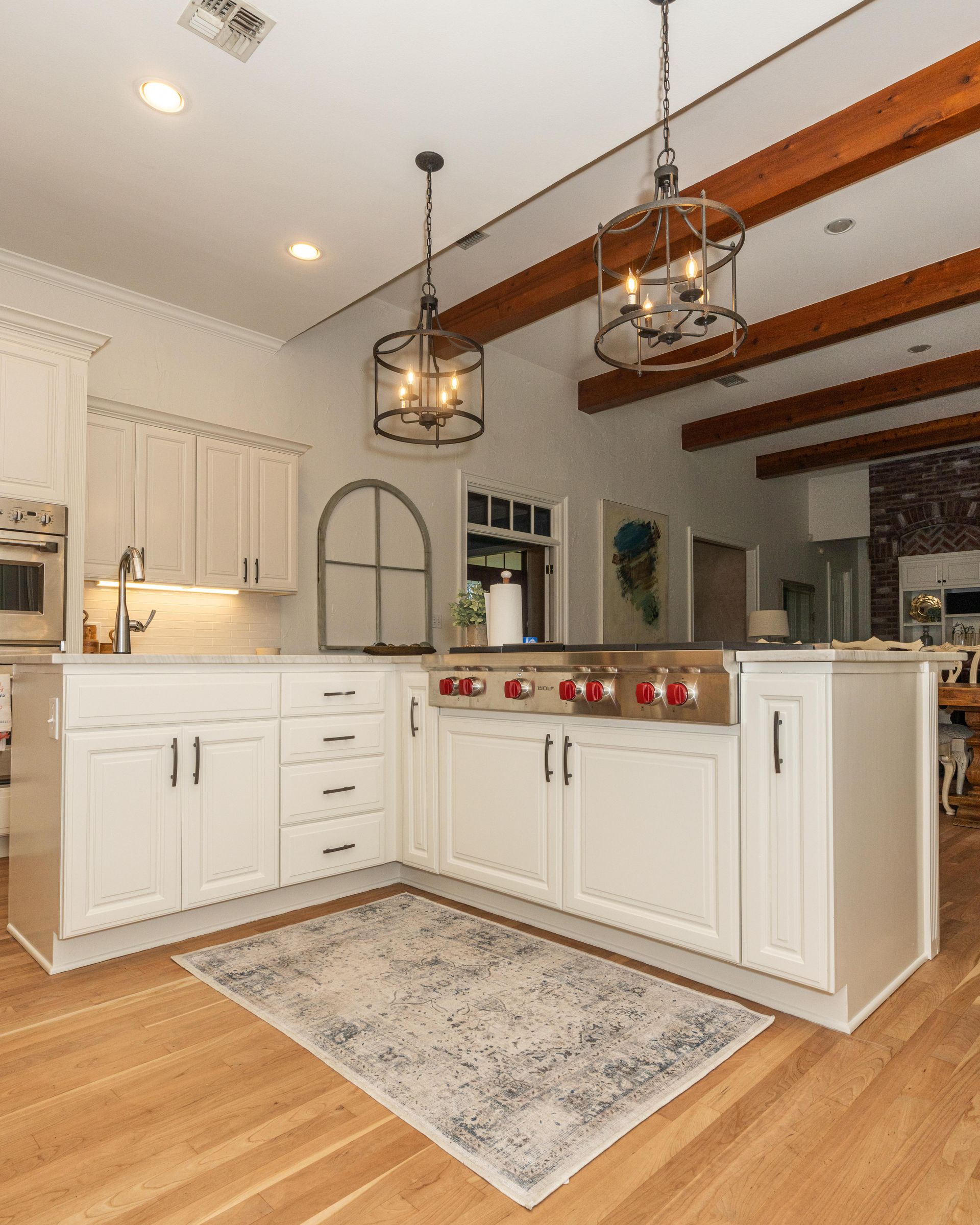 Bright white kitchen island with pendant lights, wood beams, and hardwood floors over a patterned rug