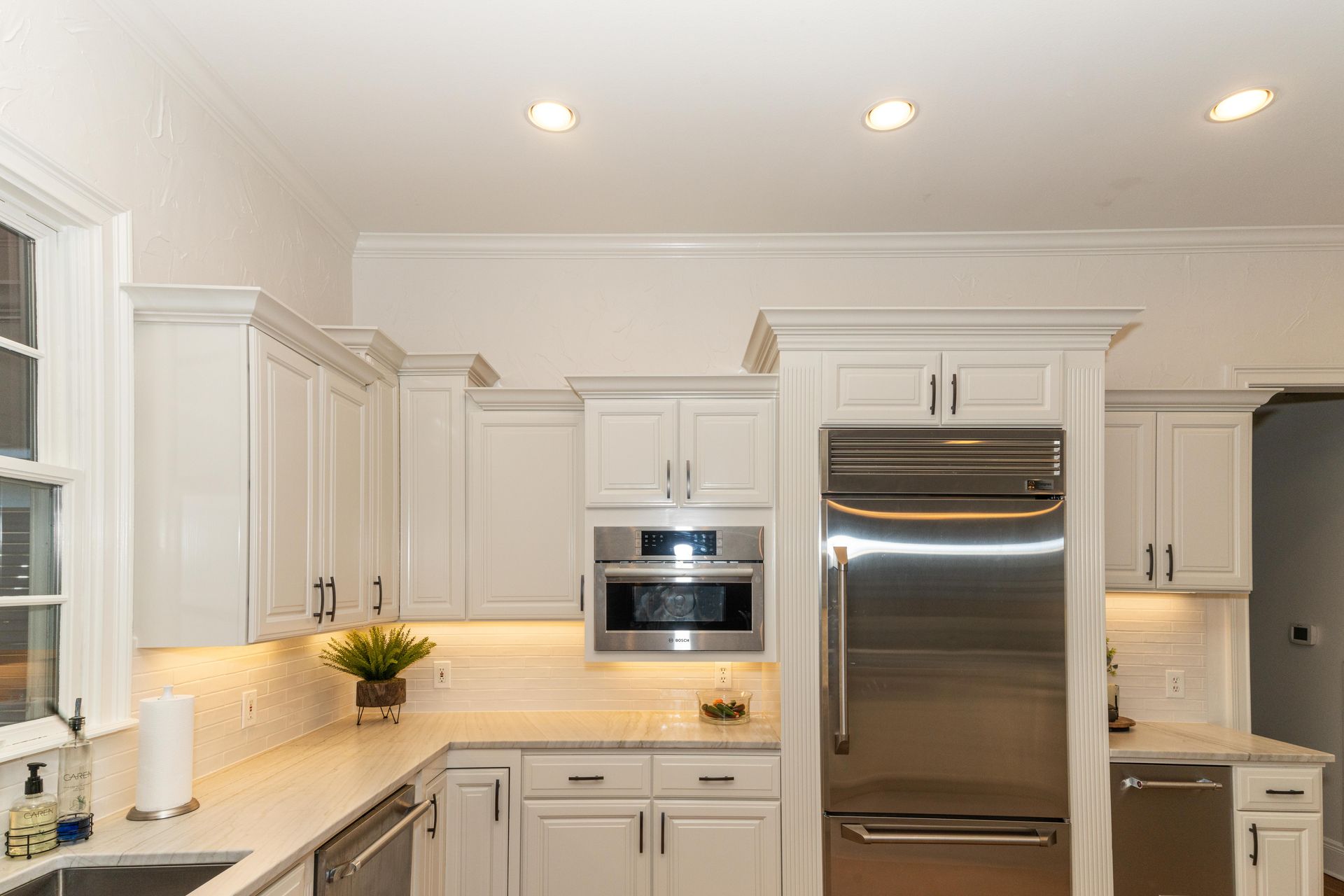Bright white modern kitchen with stainless steel refrigerator, oven, and built-in cabinets
