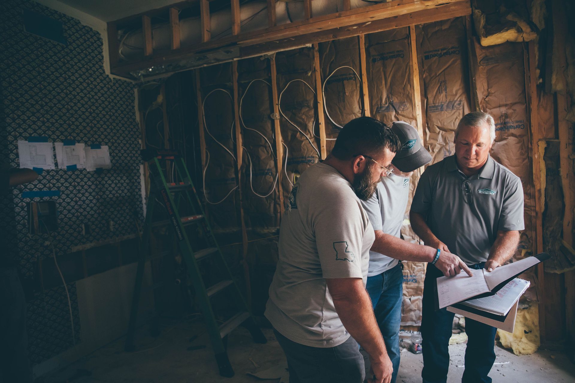Two workers reviewing plans in an unfinished room with exposed framing and tools.