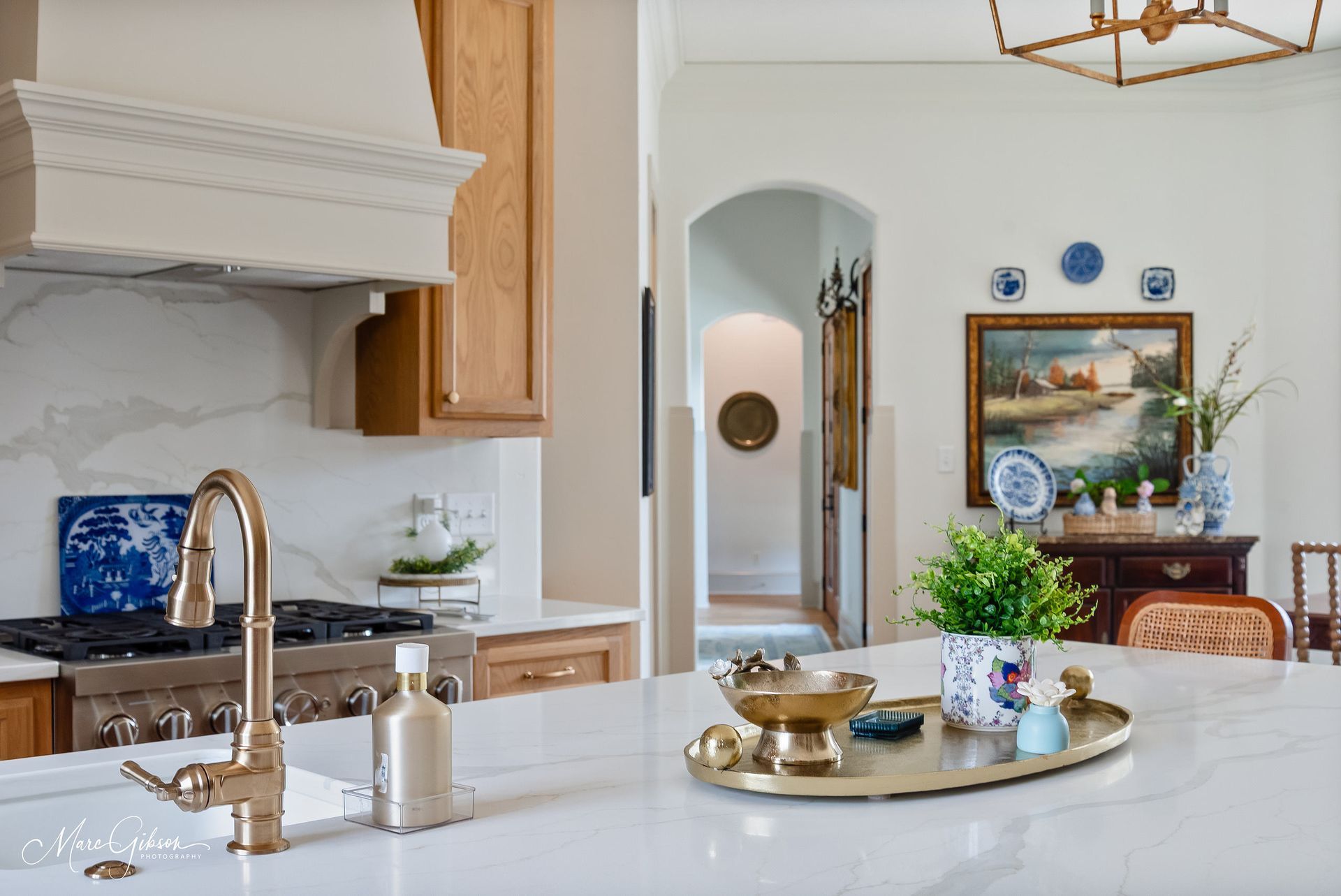 Bright white kitchen with marble island, brass faucet, wood cabinets, and a tray with flowers and decor