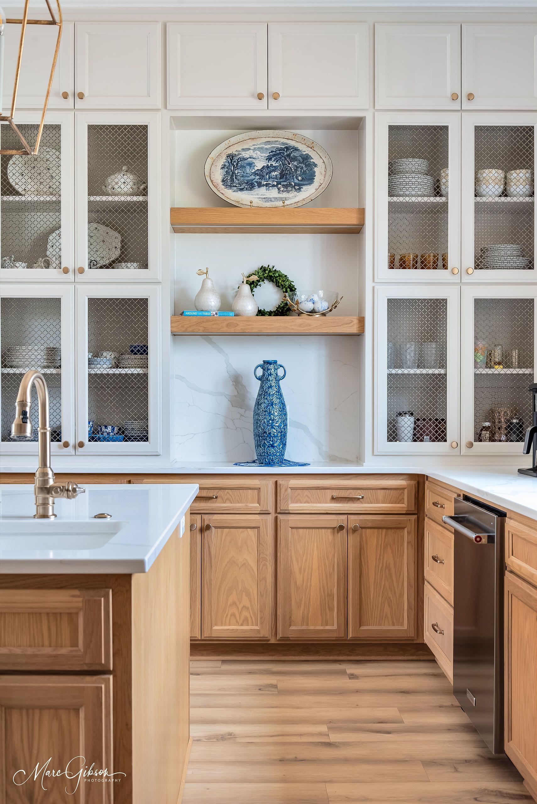 Bright kitchen with white cabinets, wooden lower cabinets, and decorative blue-and-white dishes on open shelves.