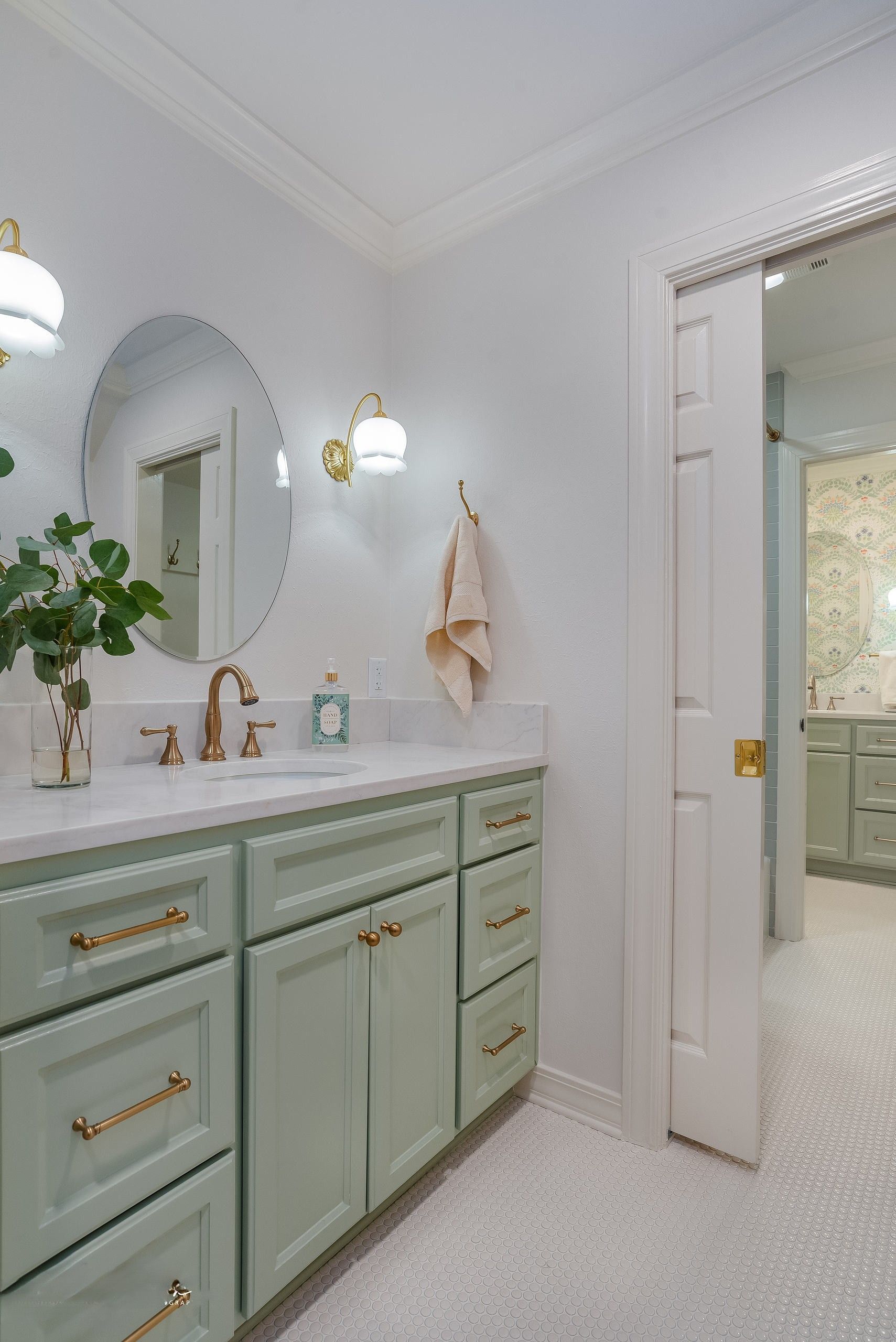 Bright bathroom with mint-green vanity, gold fixtures, arched mirror, and open doorway to shower area
