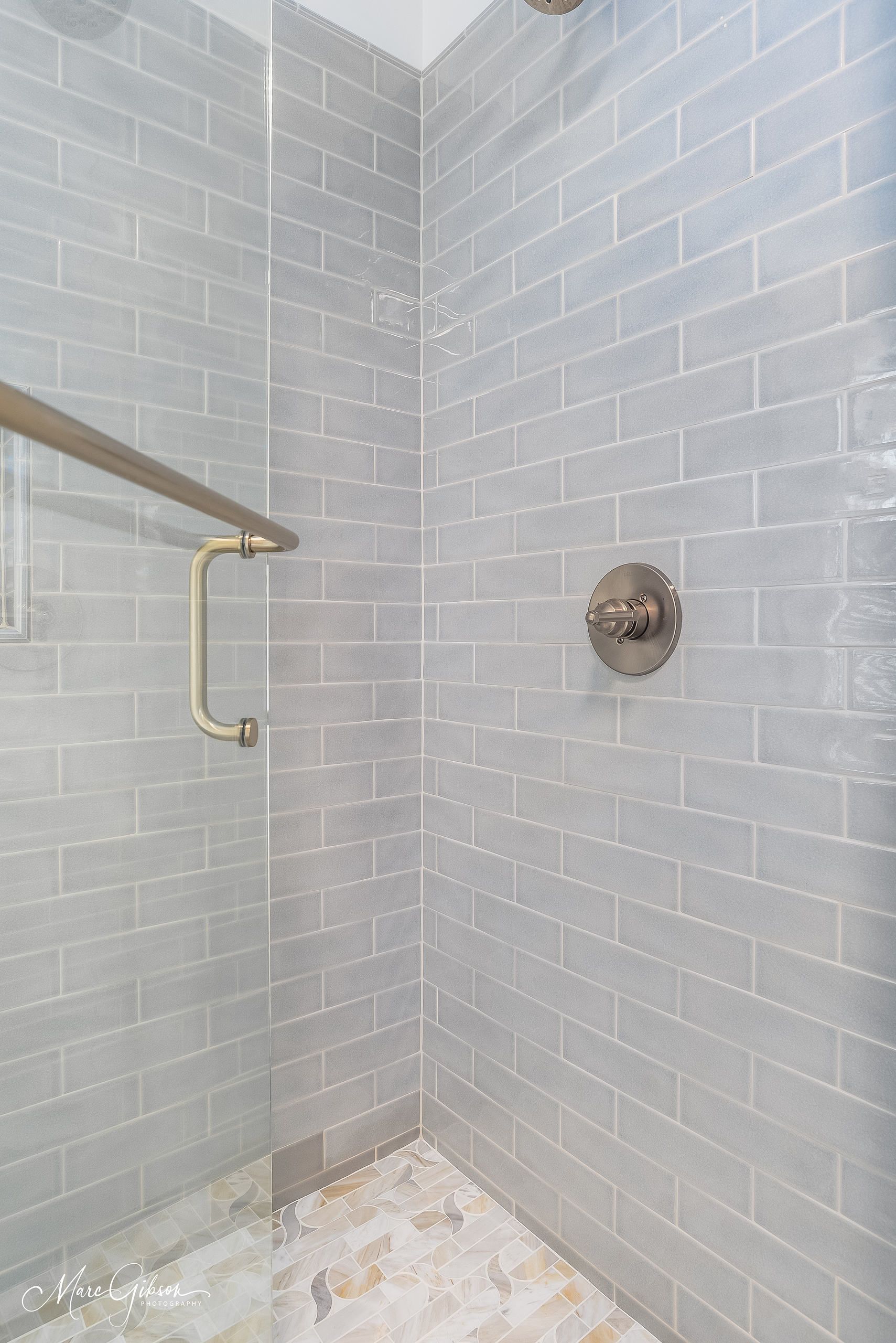 Empty tiled shower stall with a grab bar and wall-mounted shower fixture