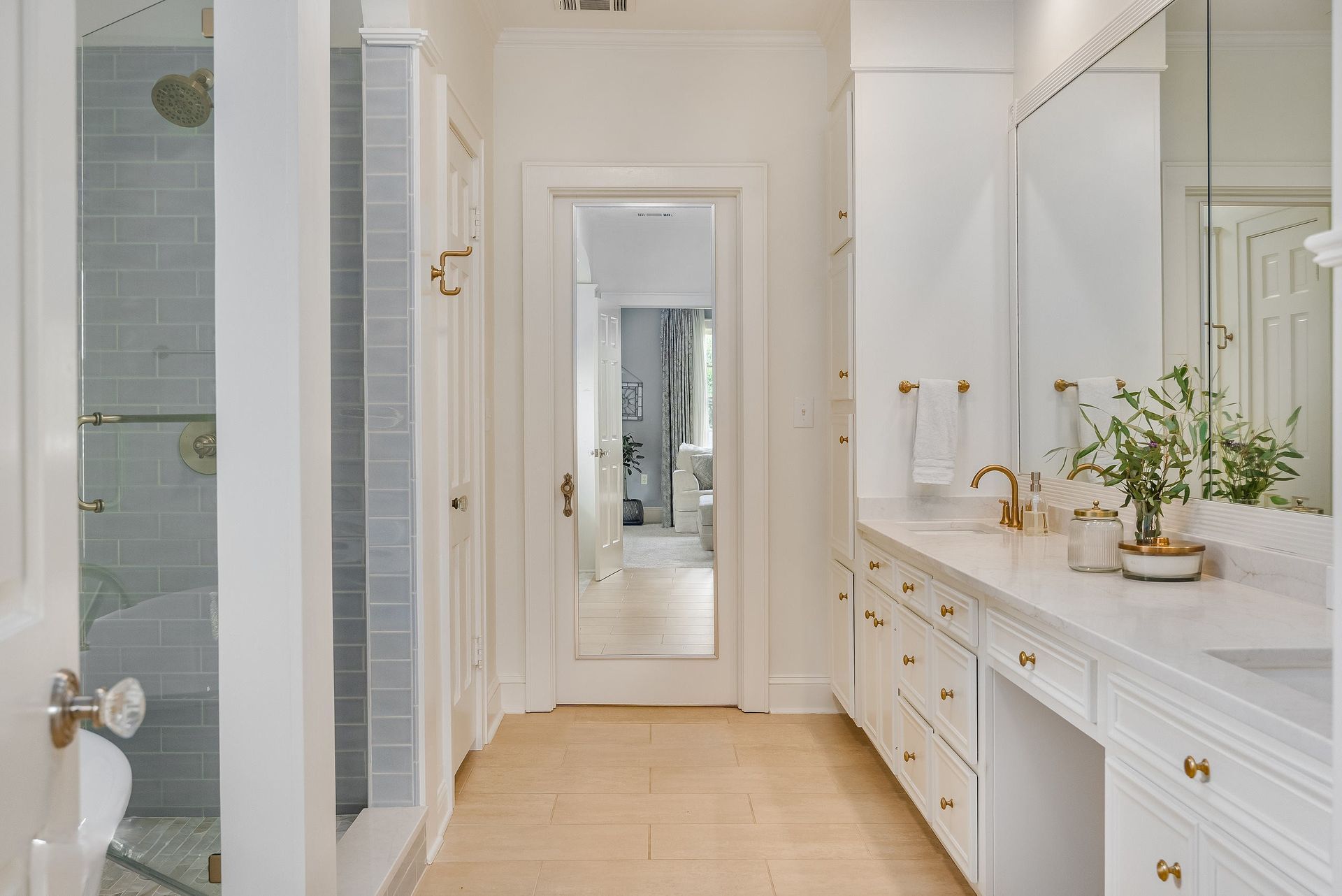 Bright bathroom with marble vanity, white door, and glass shower tiles, viewed down a narrow hallway