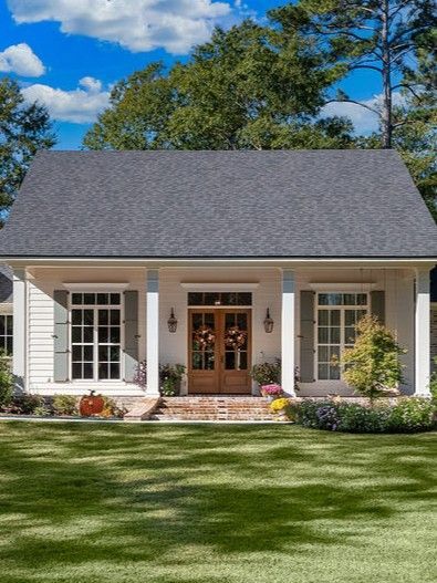 White house with gray roof, front porch, wooden double doors, and a green lawn under a blue sky