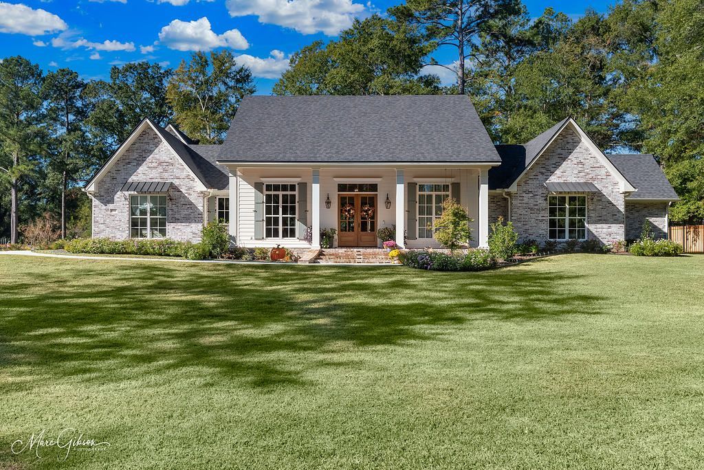 Stone house with a front porch, manicured lawn, and trees under a blue sky