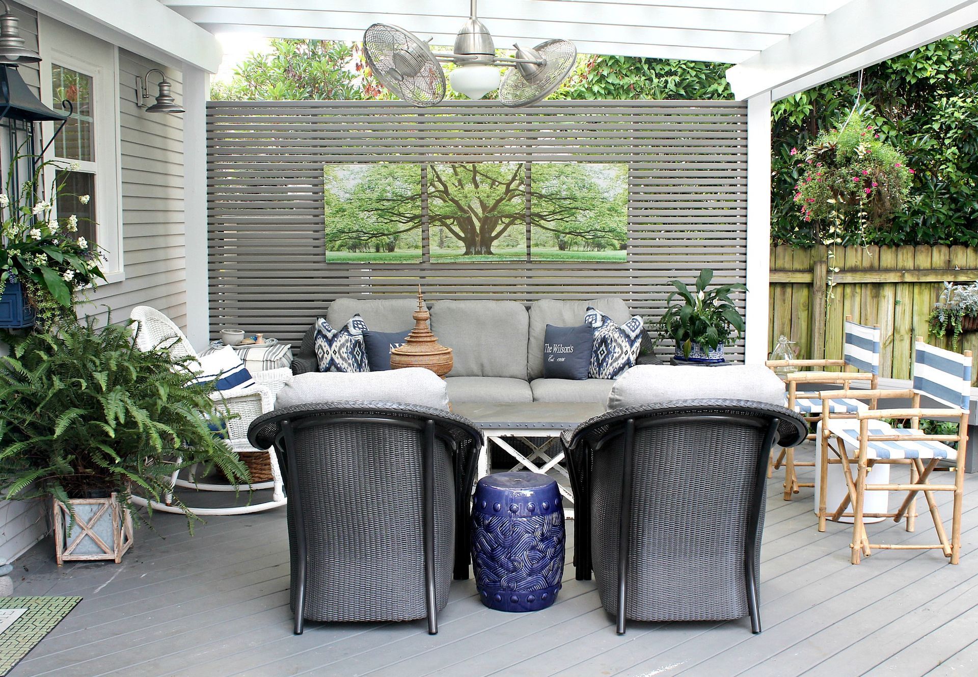 Covered patio with wicker seating, gray cushions, blue accents, and potted plants overlooking a garden