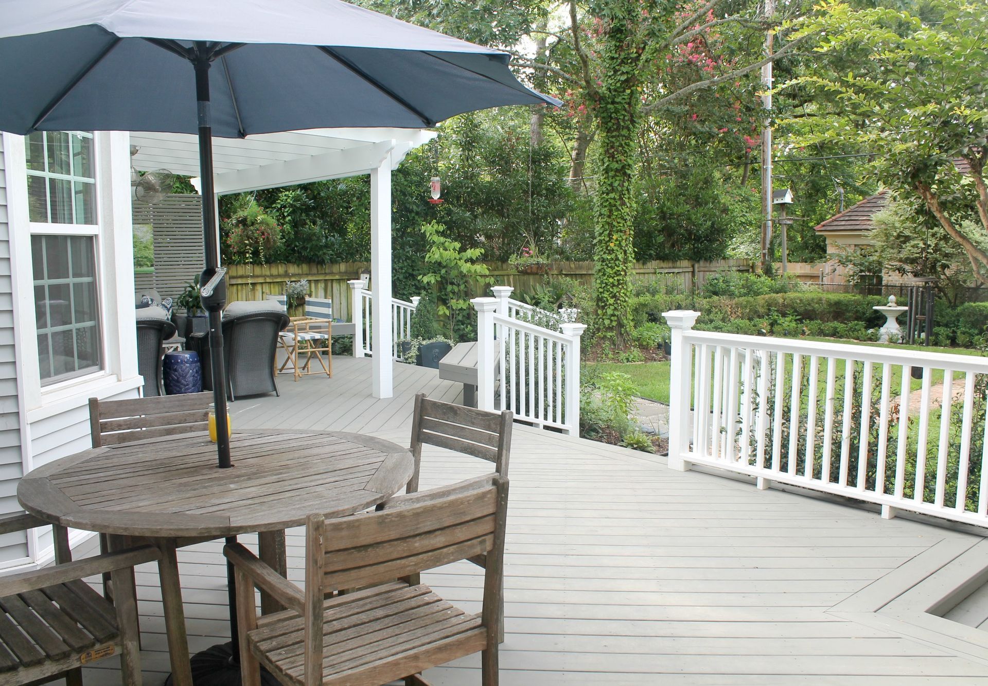 Patio deck with round table, umbrella, chairs, and white railing overlooking a garden