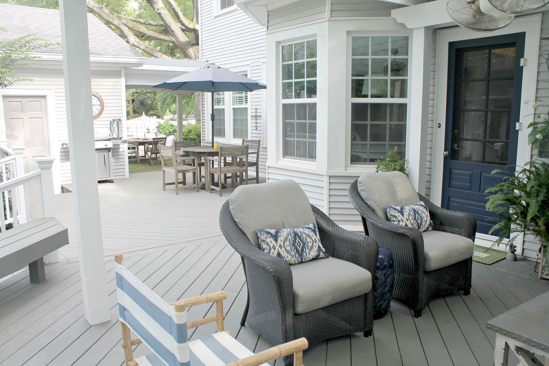 Covered porch with wicker chairs, striped cushions, and a dining table under an umbrella.