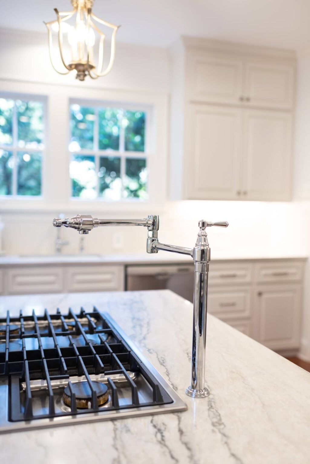 Bright modern kitchen with a chrome faucet and stovetop on a marble island, white cabinets, and window light.