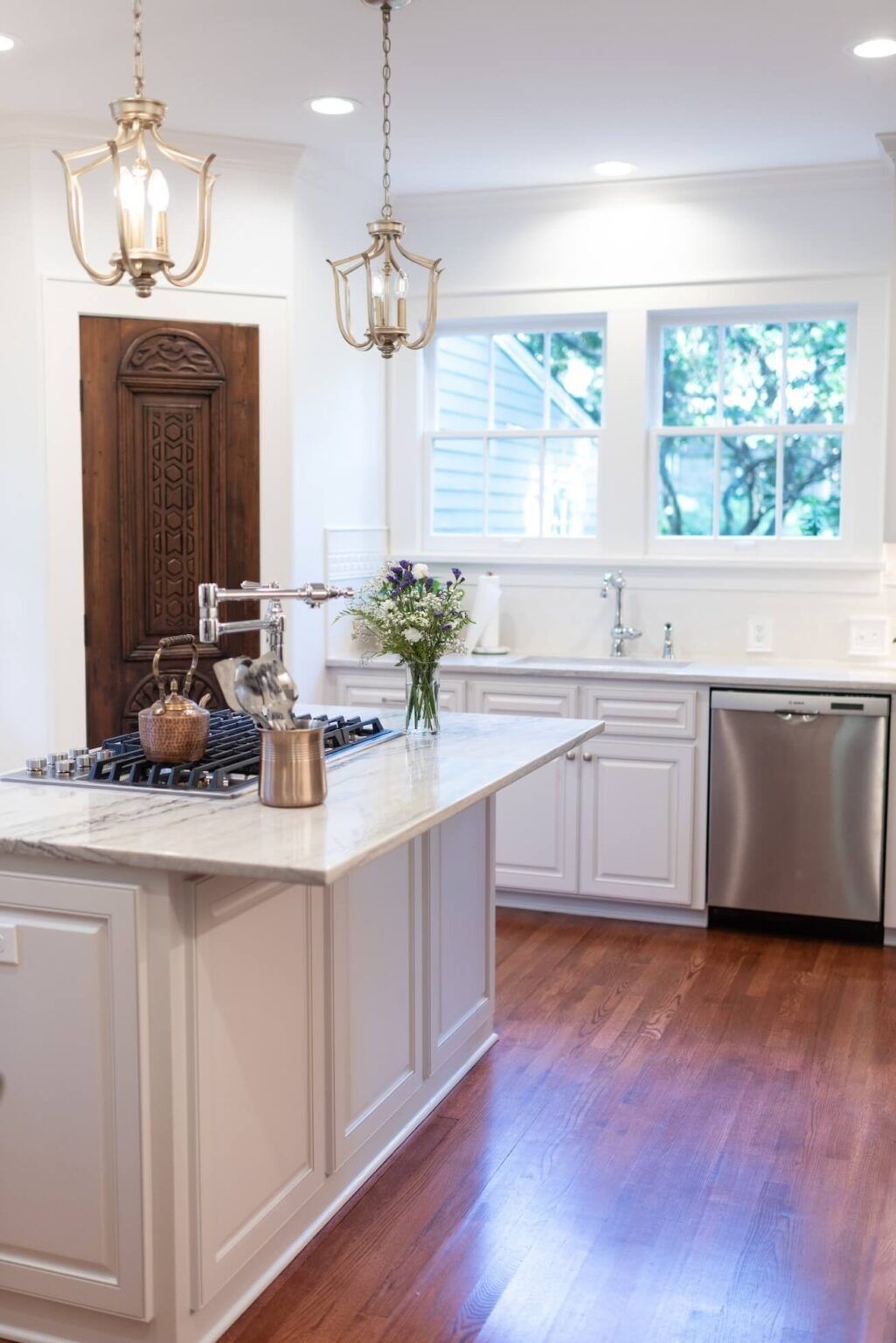 Bright modern kitchen with white cabinets, island, hardwood floors, and gold pendant lights