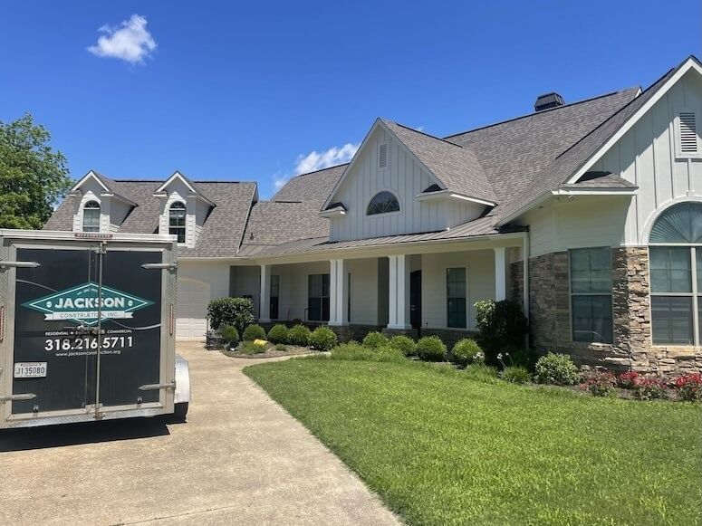 Suburban home with manicured lawn and a dumpster in the driveway under a blue sky